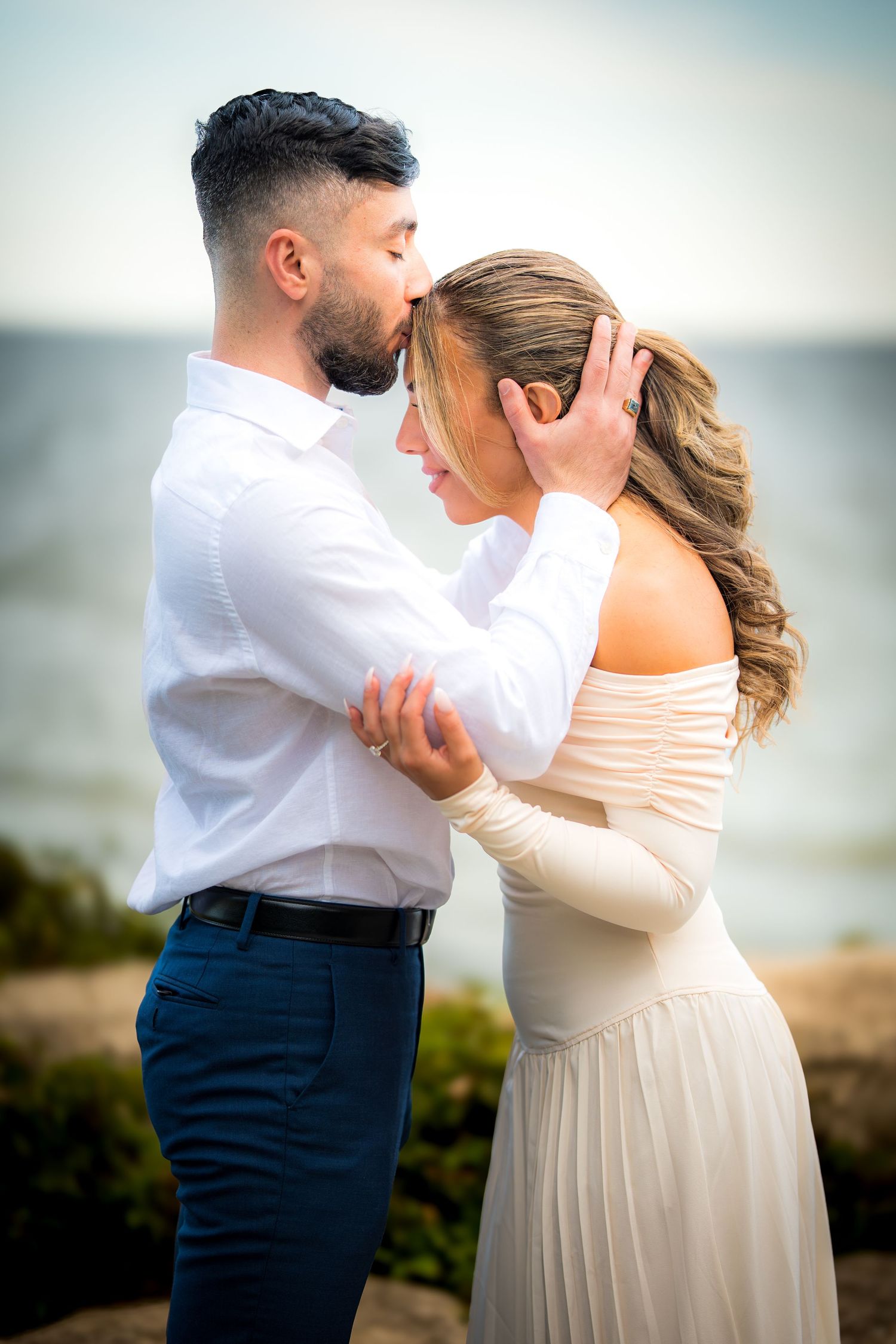 Intimate dance sequence of couple in wedding attire against blurred coastal background.