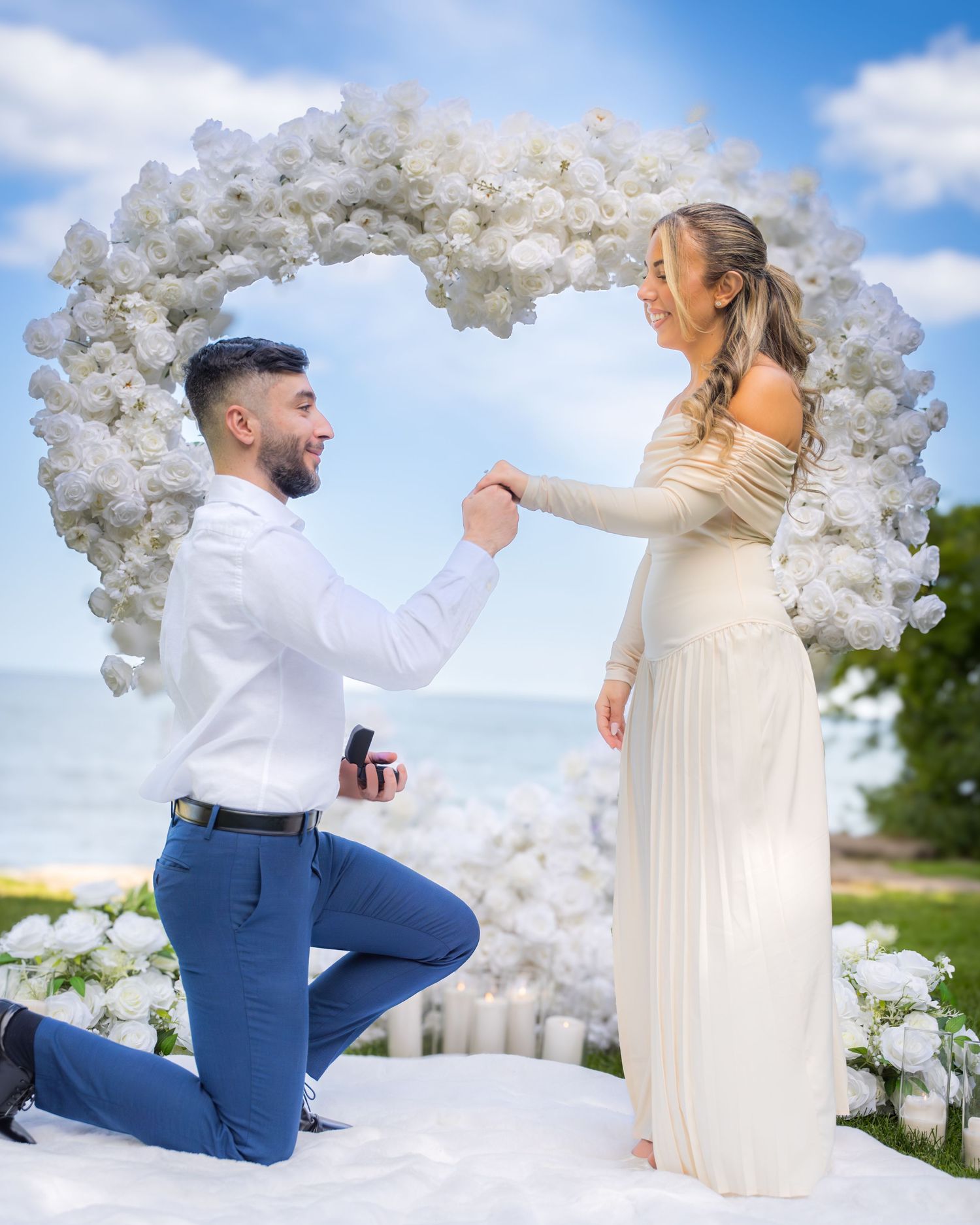 A proposal scene under a white balloon arch with scattered petals creating a romantic atmosphere.