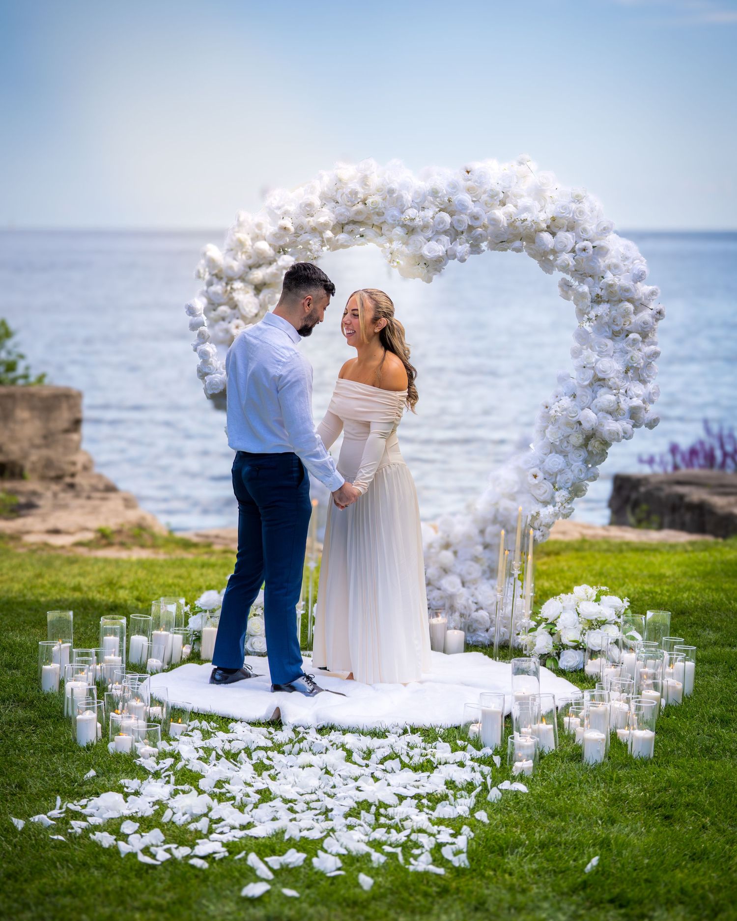 Dreamy wedding ceremony location with white floral arch and candle-lined aisle against coastal backdrop.