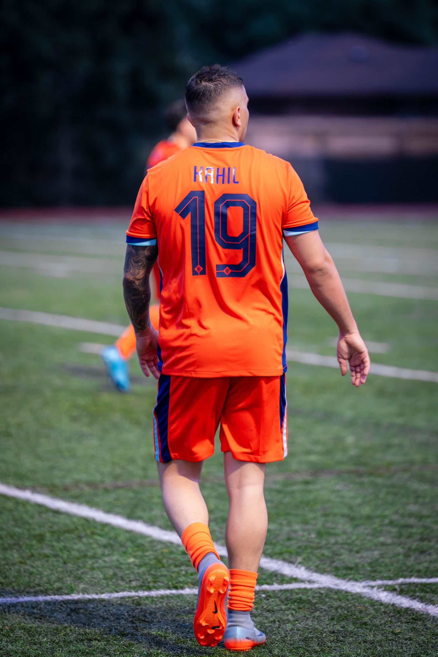 Player in bright orange uniform runs along sideline during soccer match.