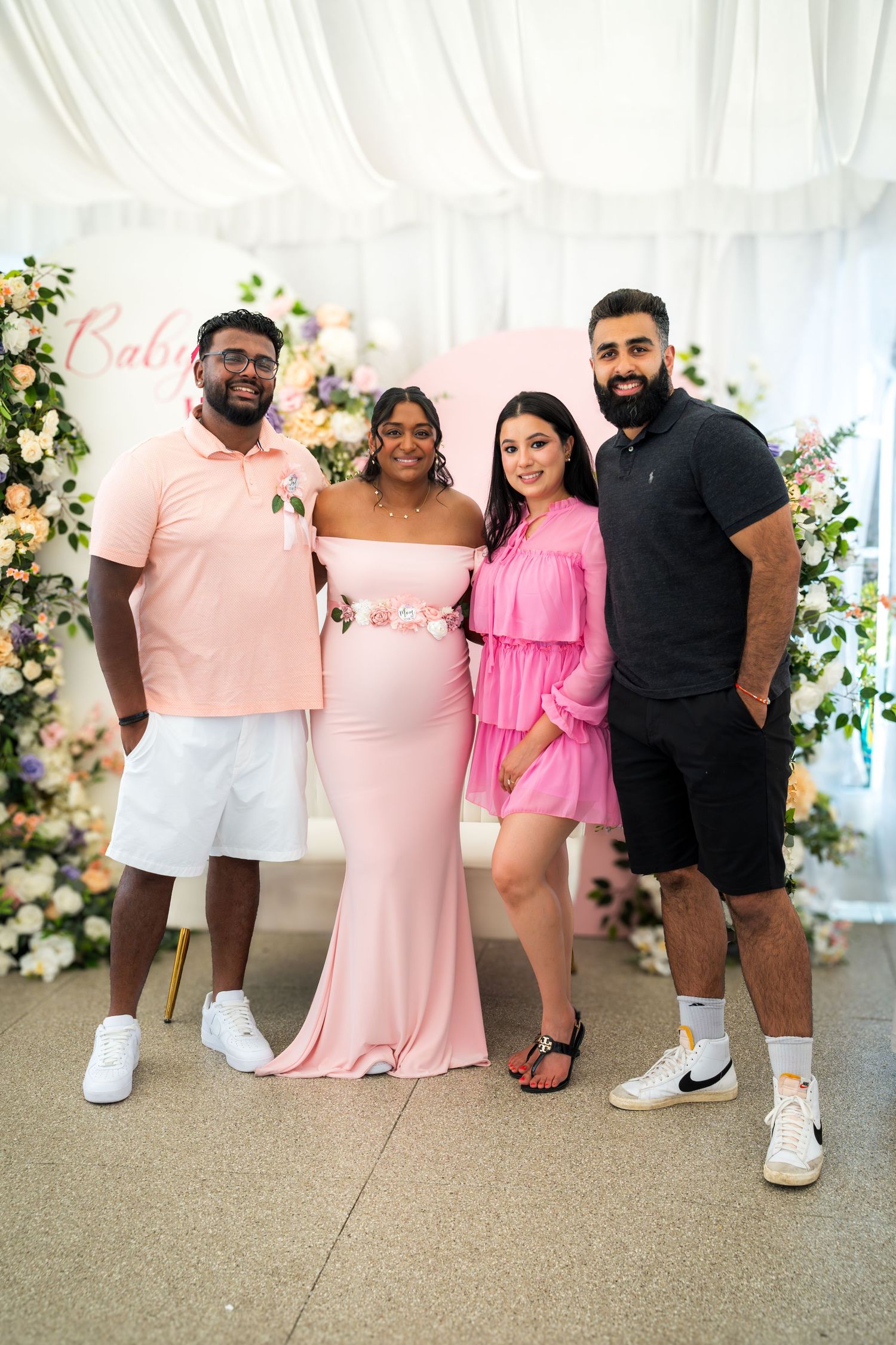 Four guests pose together at baby shower with pink and floral decorations.