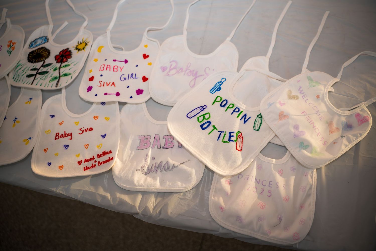 Decorated baby bibs arranged in a line showing various artistic designs and messages.