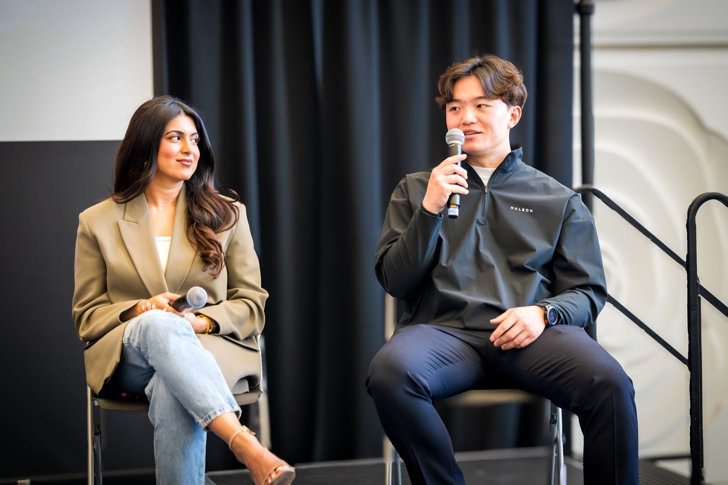 Professional speakers seated in casual conversation during conference panel discussion.
