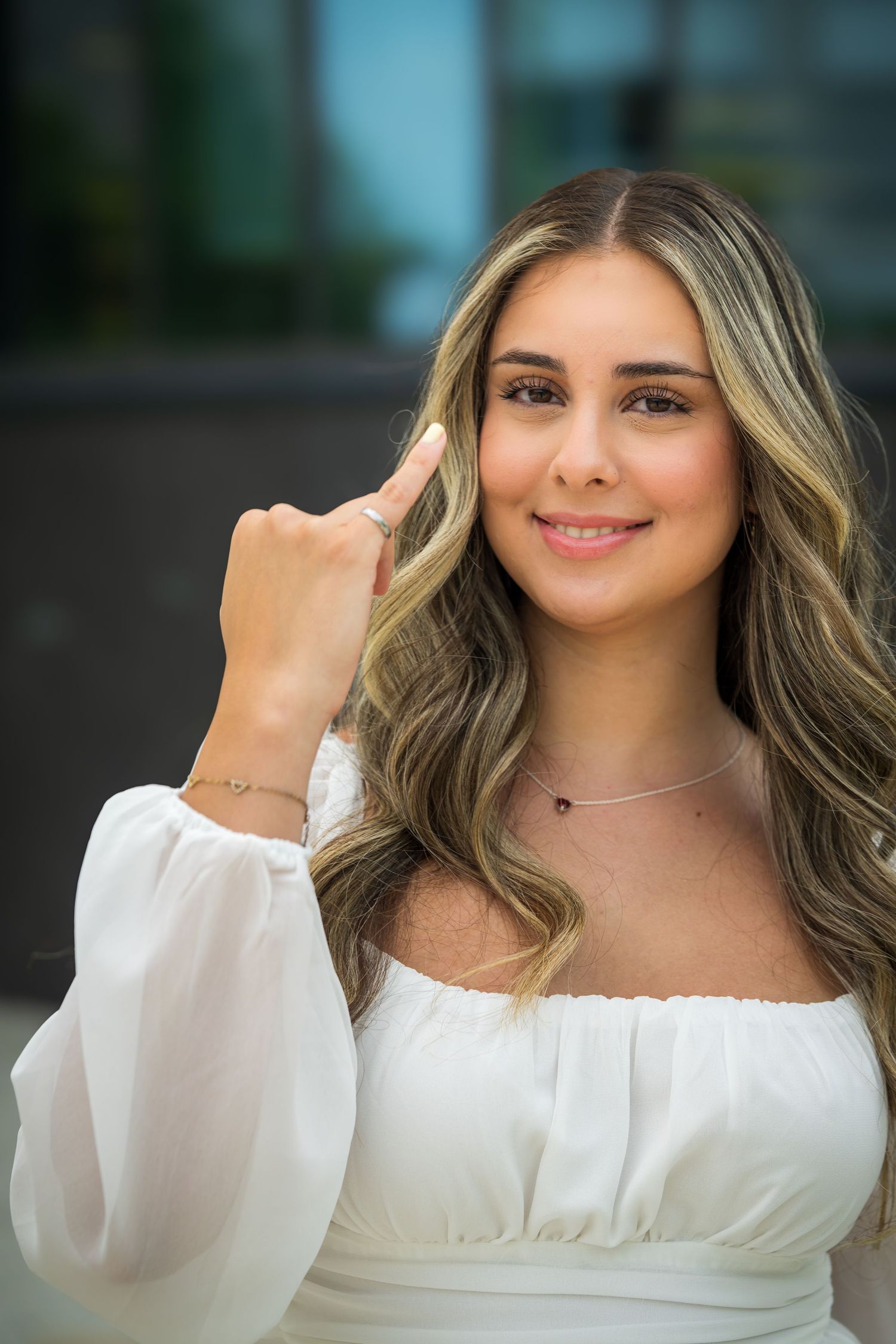 Portrait of graduate wearing white dress and delicate necklace with soft natural makeup.