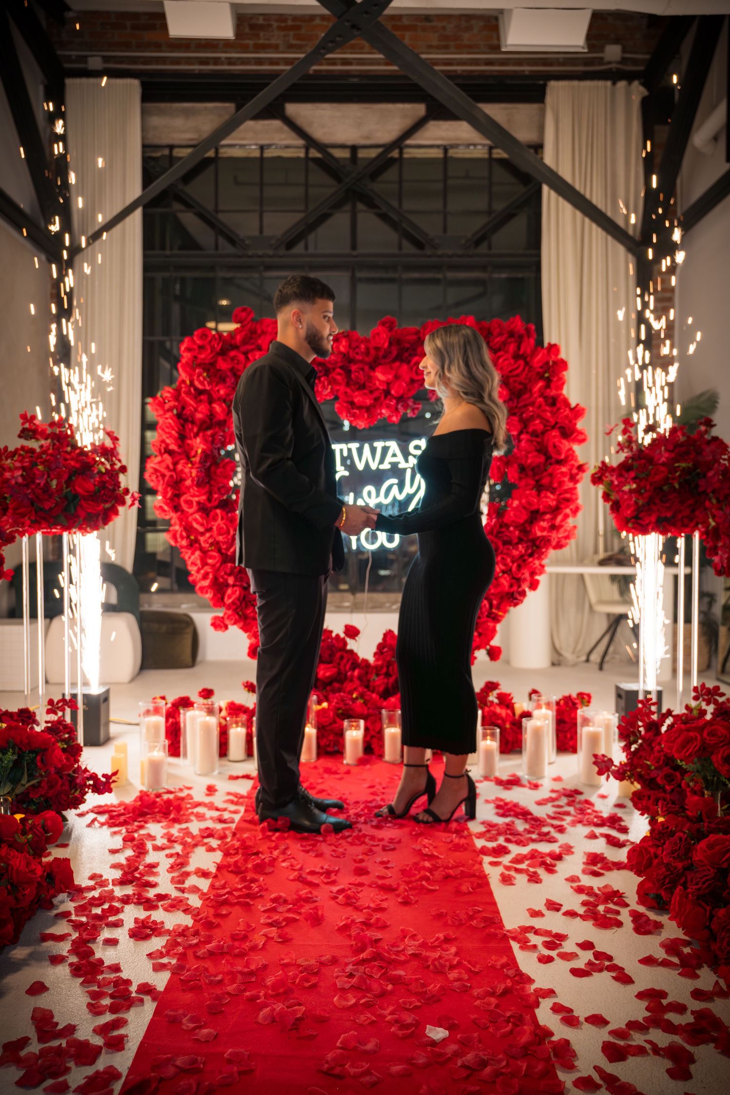 Dramatic wide angle view of proposal setting with red rose walls and scattered petals.