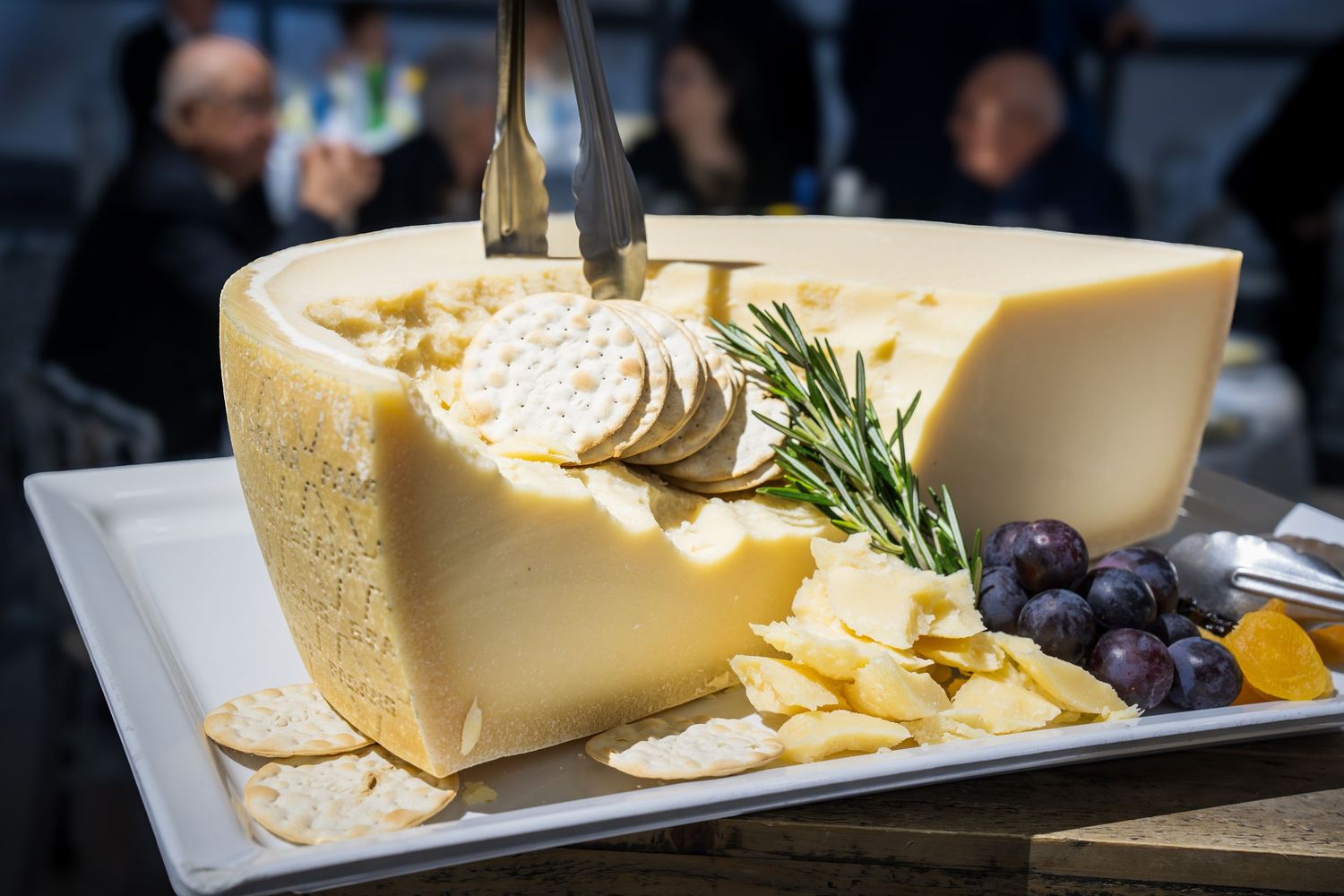Large wedge of aged cheese served with crackers, grapes, and rosemary on white platter.