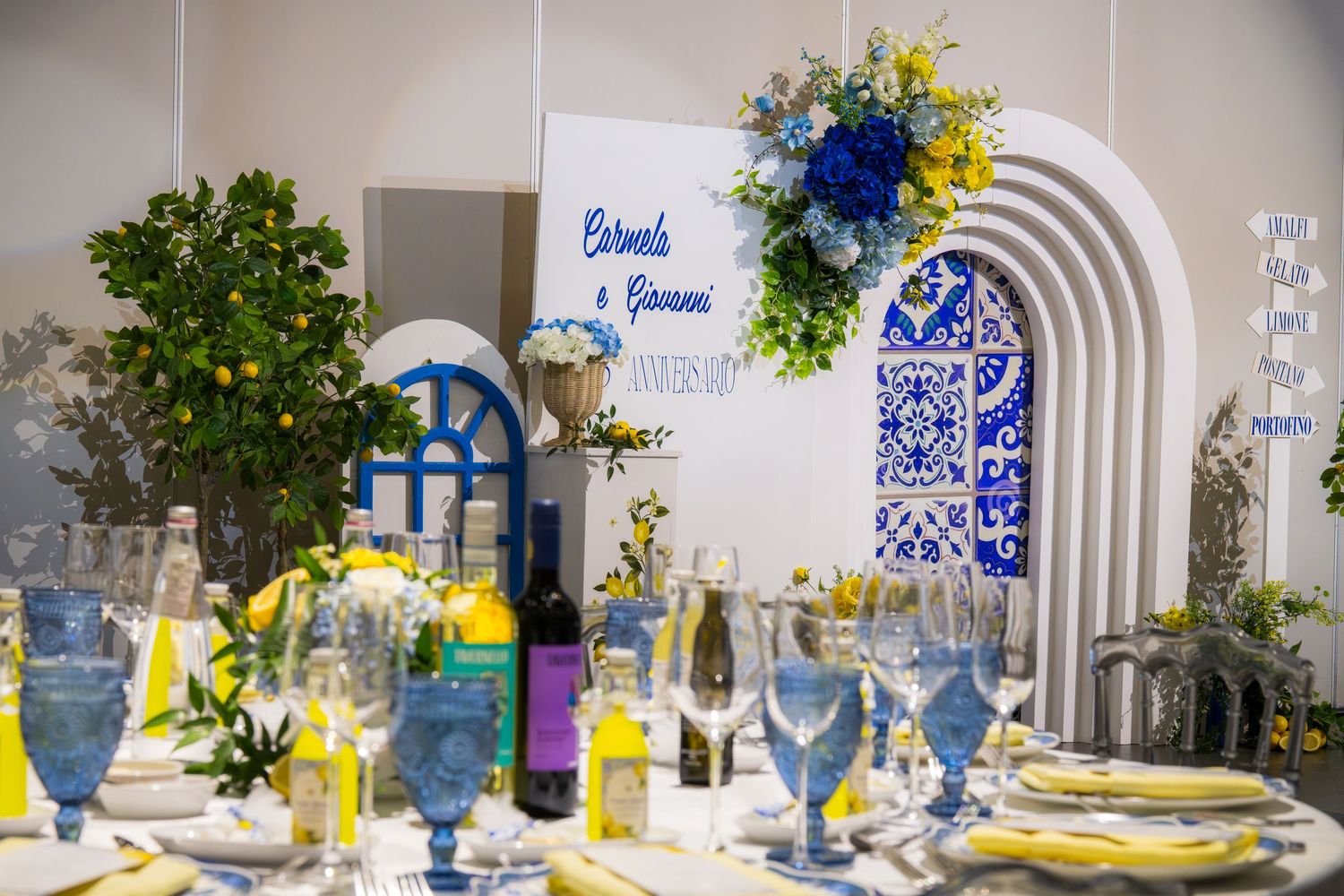 Elegant blue and yellow Italian-themed anniversary table setting with arched decor and lemon tree centerpiece.
