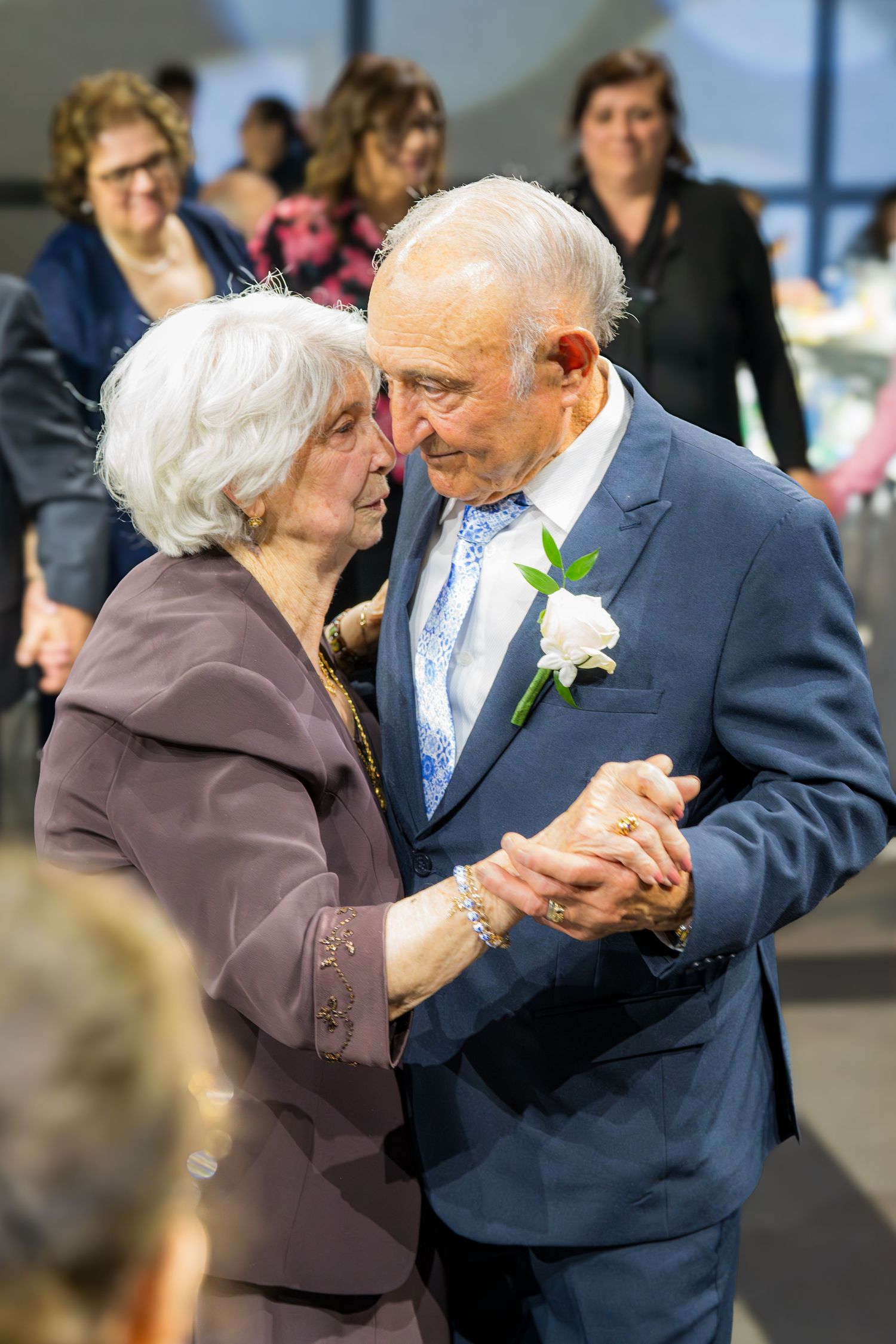 Elderly couple sharing a romantic dance at a formal celebration, man wearing blue suit with white boutonniere.