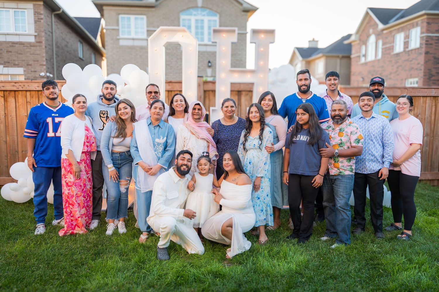Large family group poses together on a lawn in front of white balloon decorations at a gender reveal.