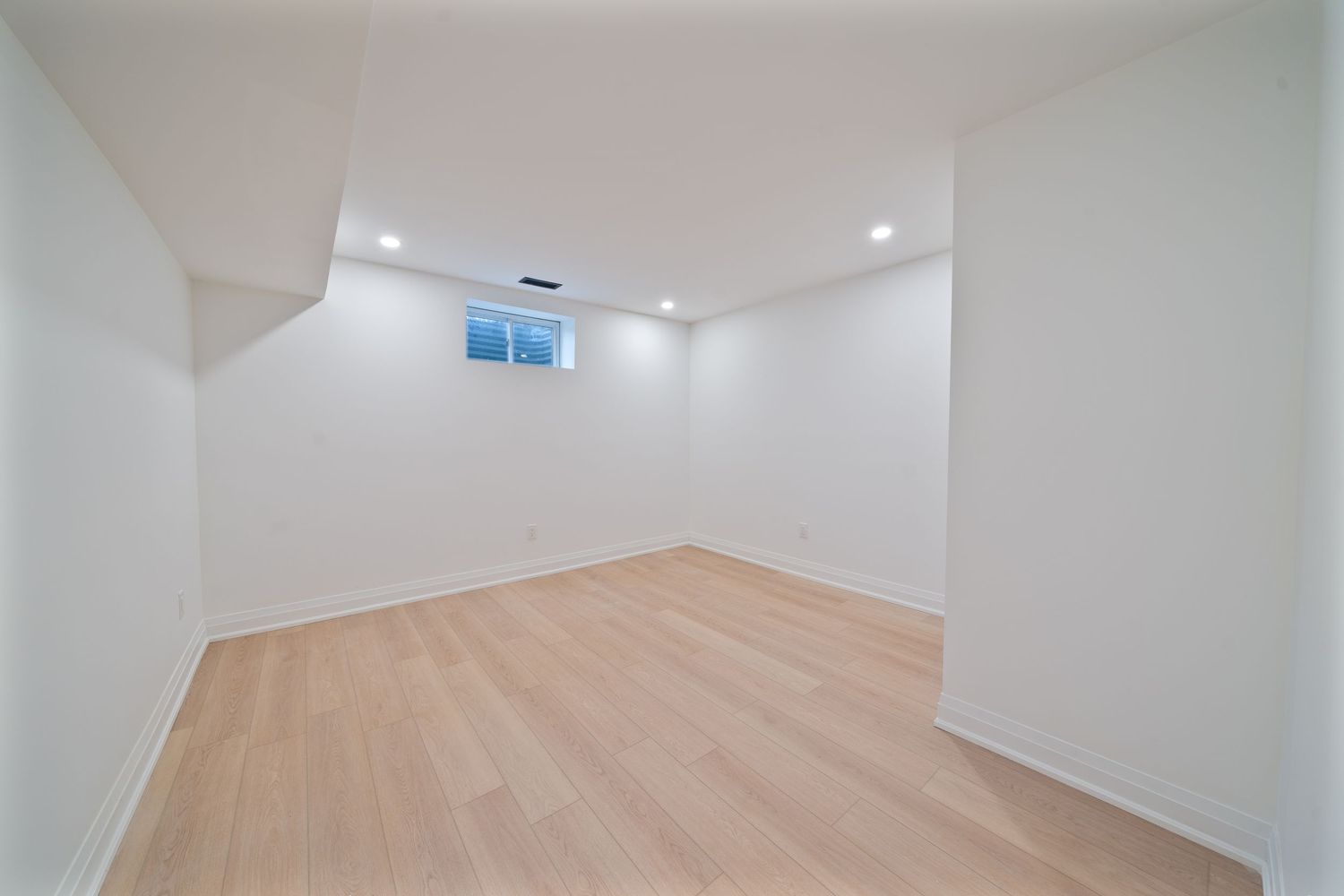 Modern white hallway with light hardwood flooring and recessed lighting extends into a bright open space.