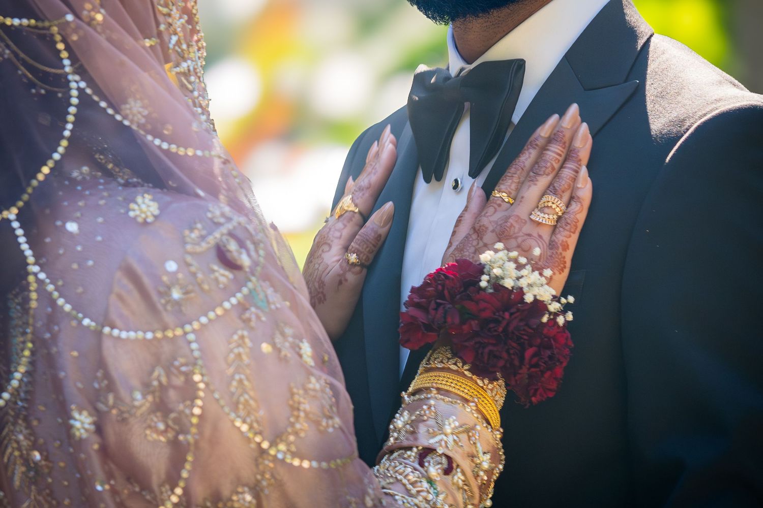 Close-up of decorated hands and formal attire details at South Asian wedding ceremony.