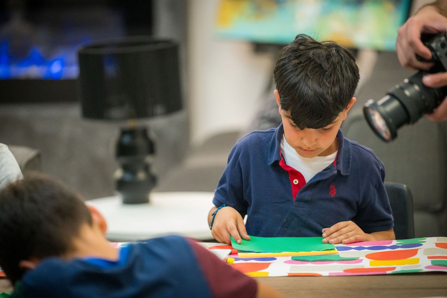 Young boy carefully works with colorful paper shapes during a creative art activity.