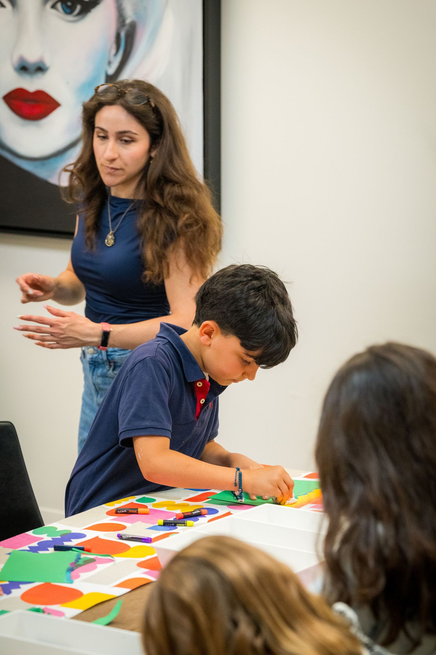 A female instructor gestures while a boy works on a colorful paper collage art project.