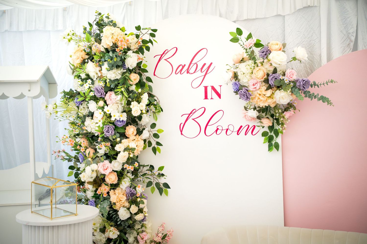Decorative floral installation with 'Bloom' text in pink script against white and pink wall.