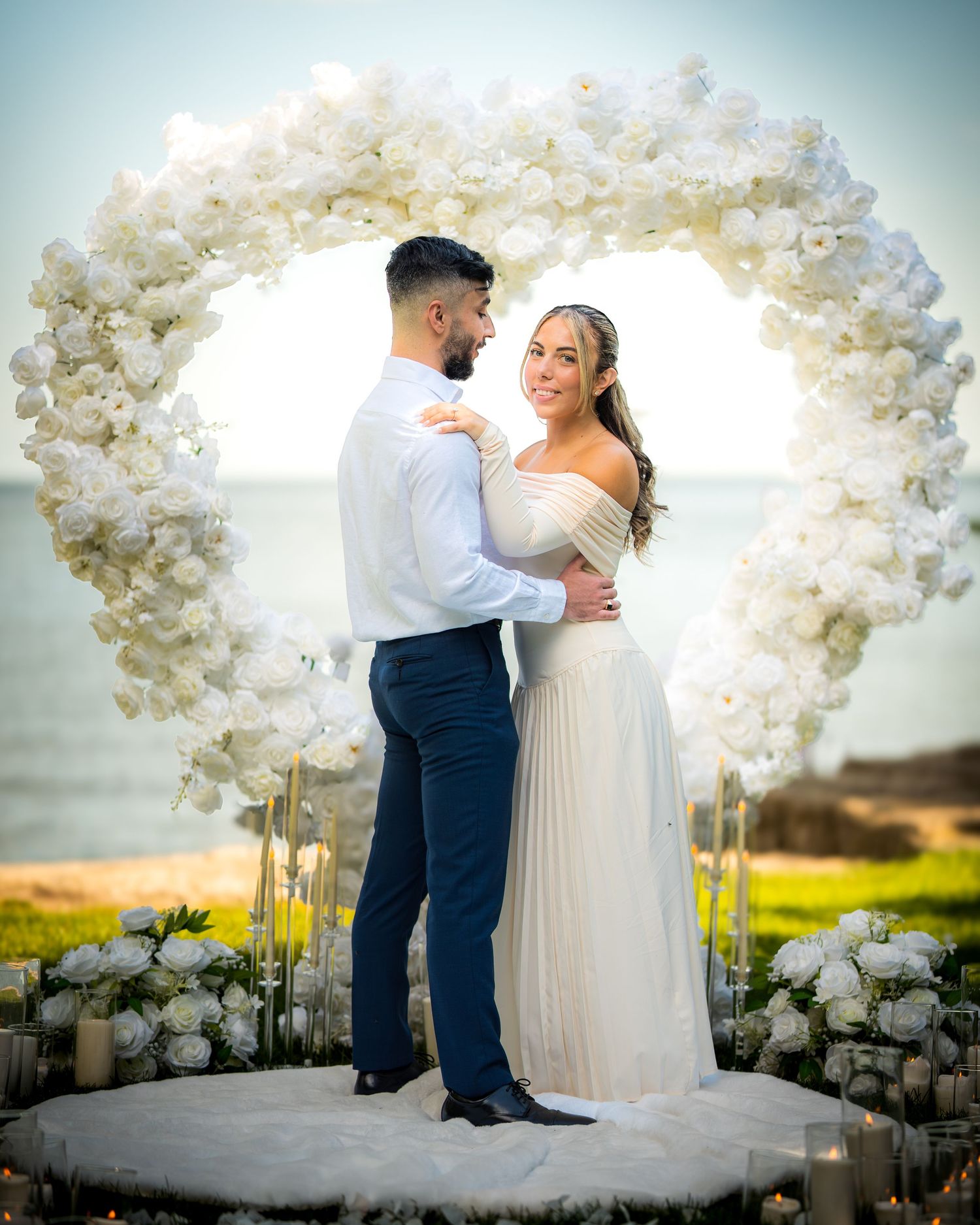 Wedding couple dancing beneath white floral arches at sunset.