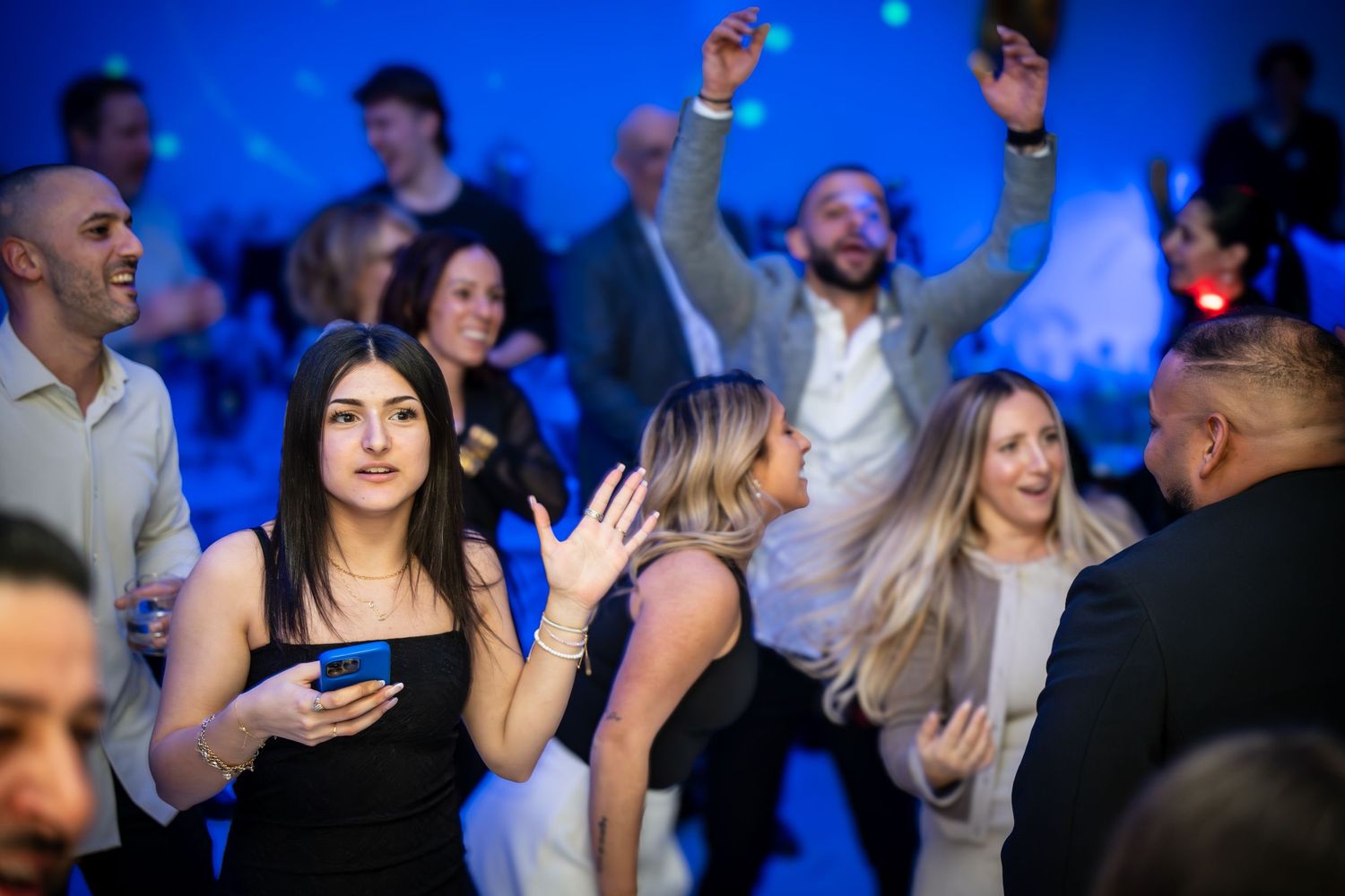 People dancing and celebrating at a lively event with blue lighting and a festive atmosphere.