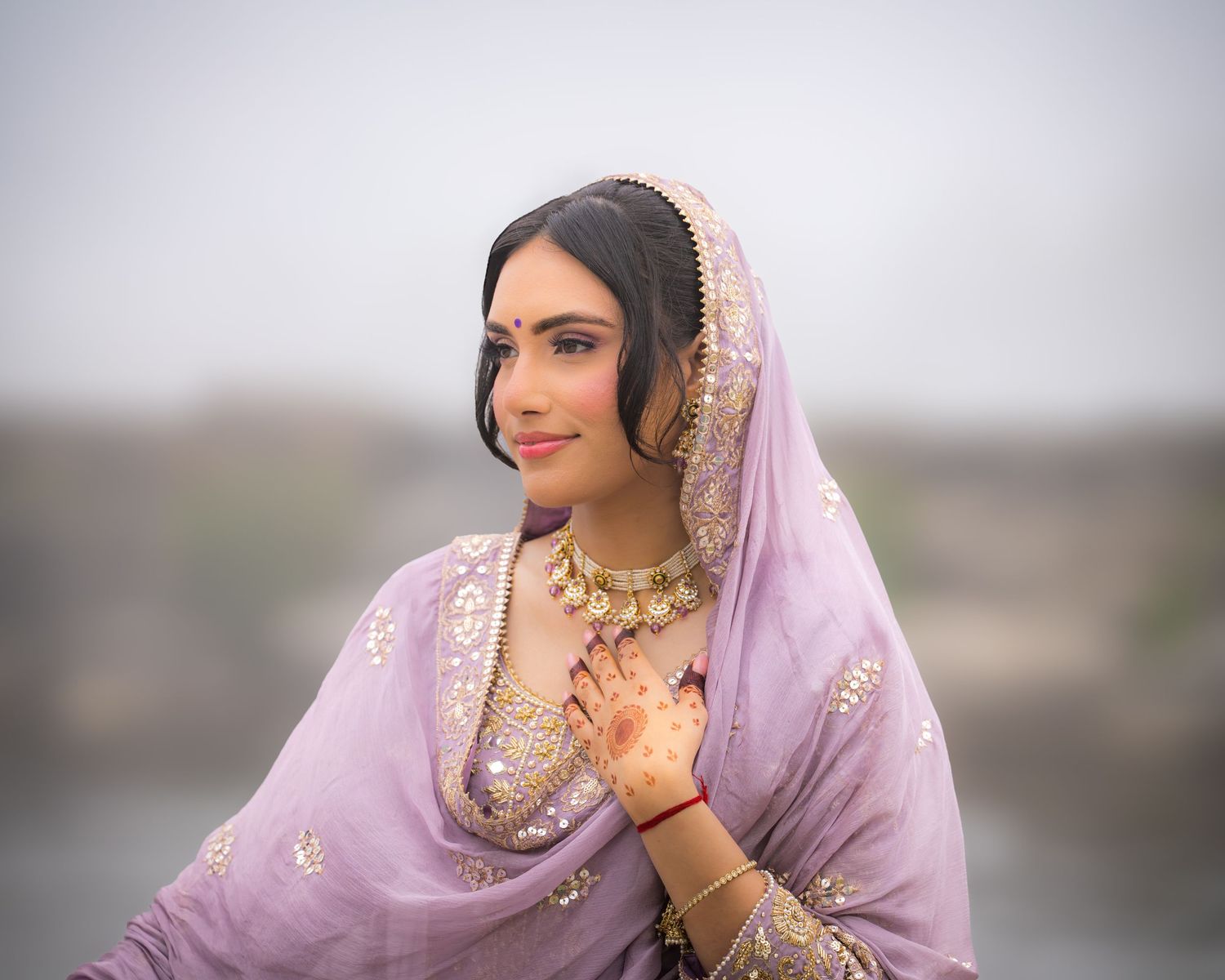 A person in an ornate purple outfit with traditional jewelry poses gracefully outdoors.