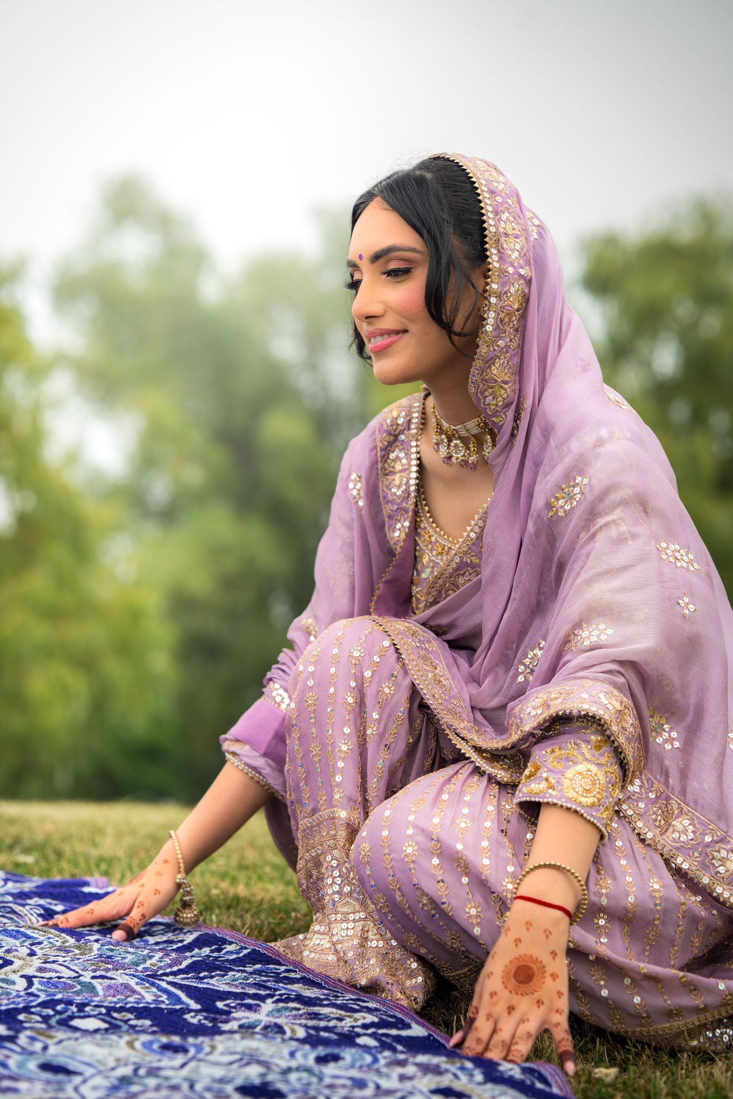 Elegant lavender and gold embroidered outfit shown against blue patterned textile outdoors.