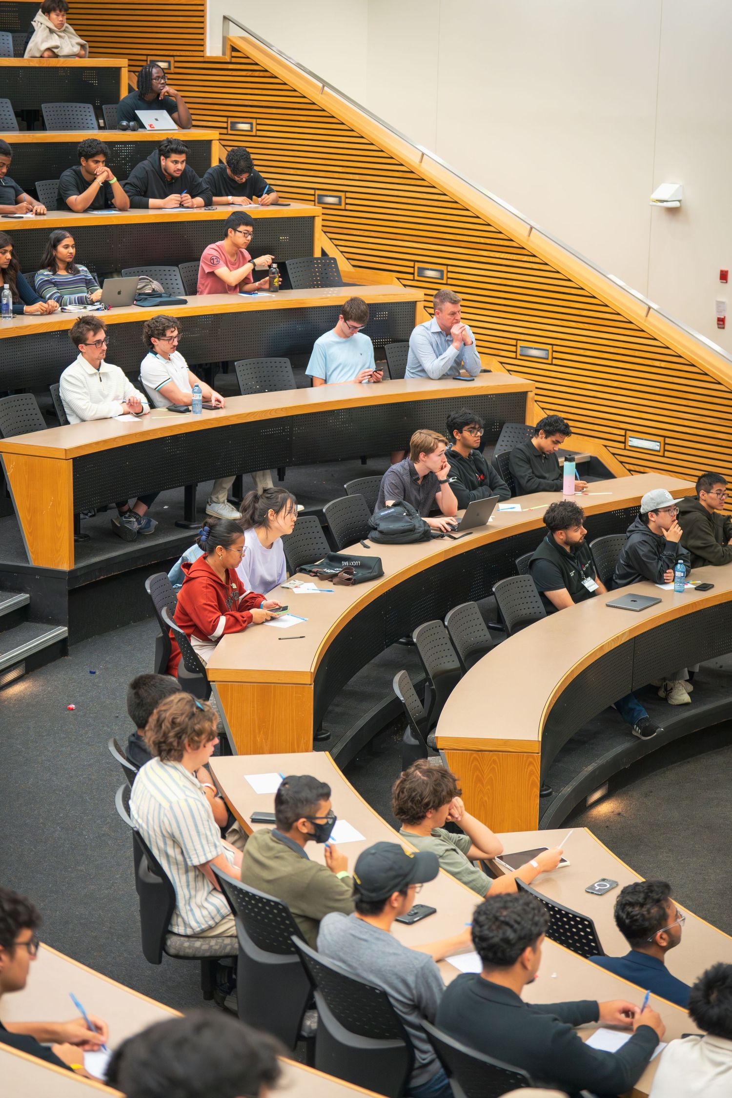 Students attend a lecture in a tiered classroom with wooden accents and modern furnishings.