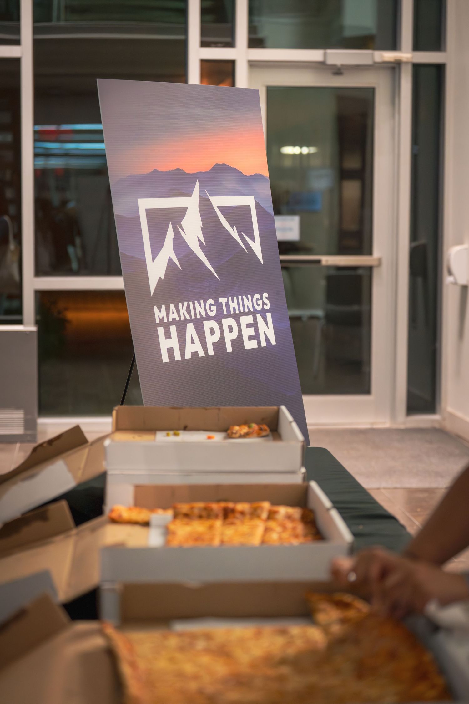 Pizza boxes and 'Making Things Happen' branded signage displayed on a table at an event.