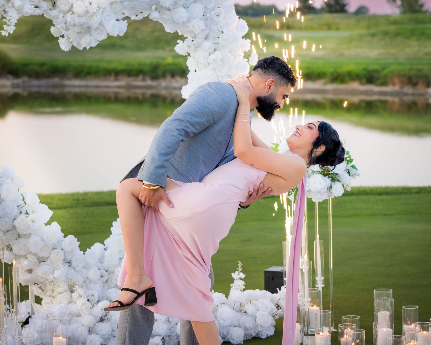 A romantic dip pose photographed with white floral decorations and glowing candles at dusk.