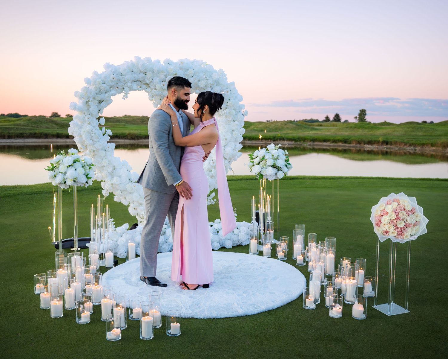 Wedding celebration on golf course featuring white floral arch and path lined with glowing lanterns.