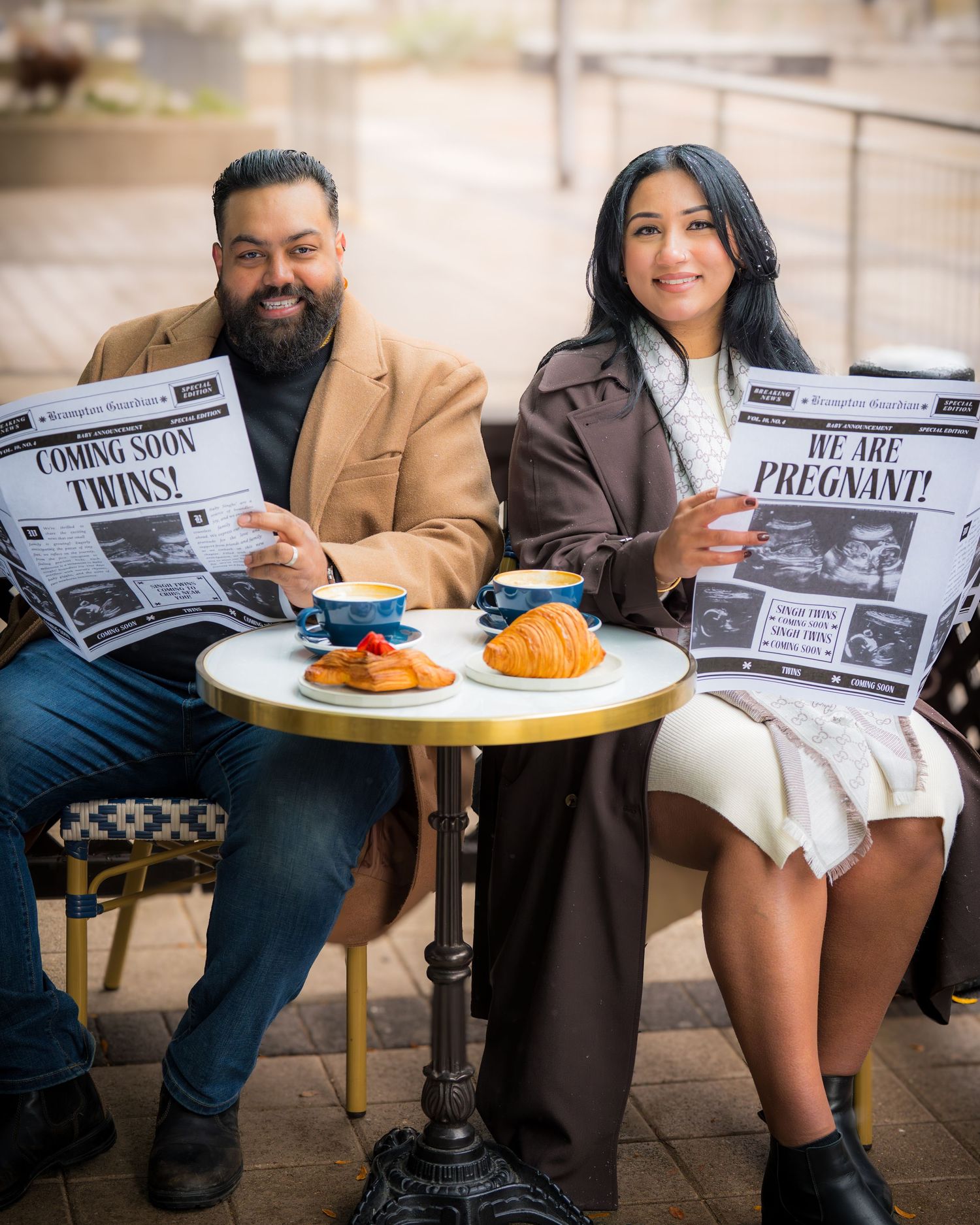 Couple at cafe table holding newspaper headlines announcing pregnancy in creative pregnancy announcement photoshoot.
