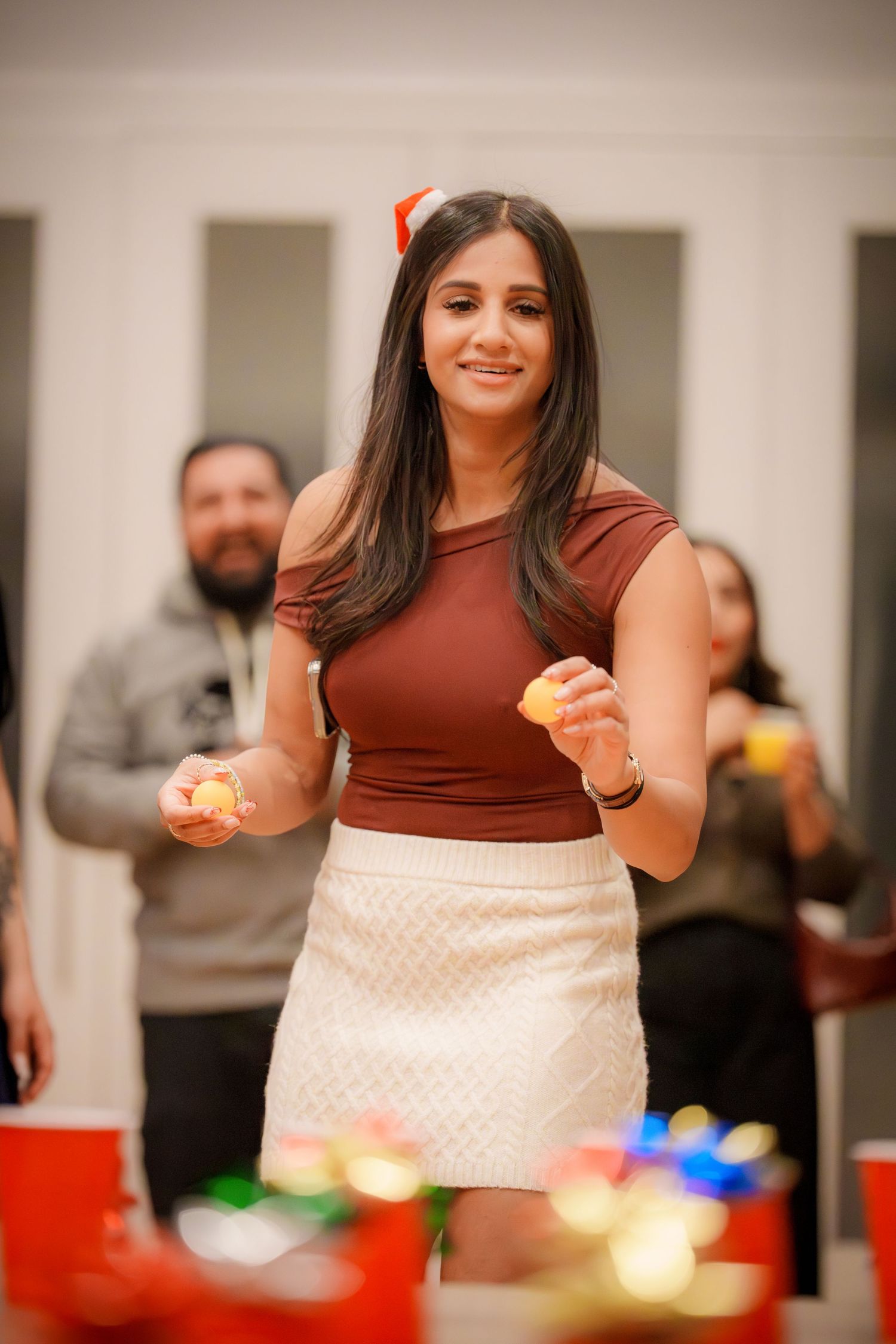 Person in brown top and white skirt enjoying food and drinks at a festive indoor gathering.