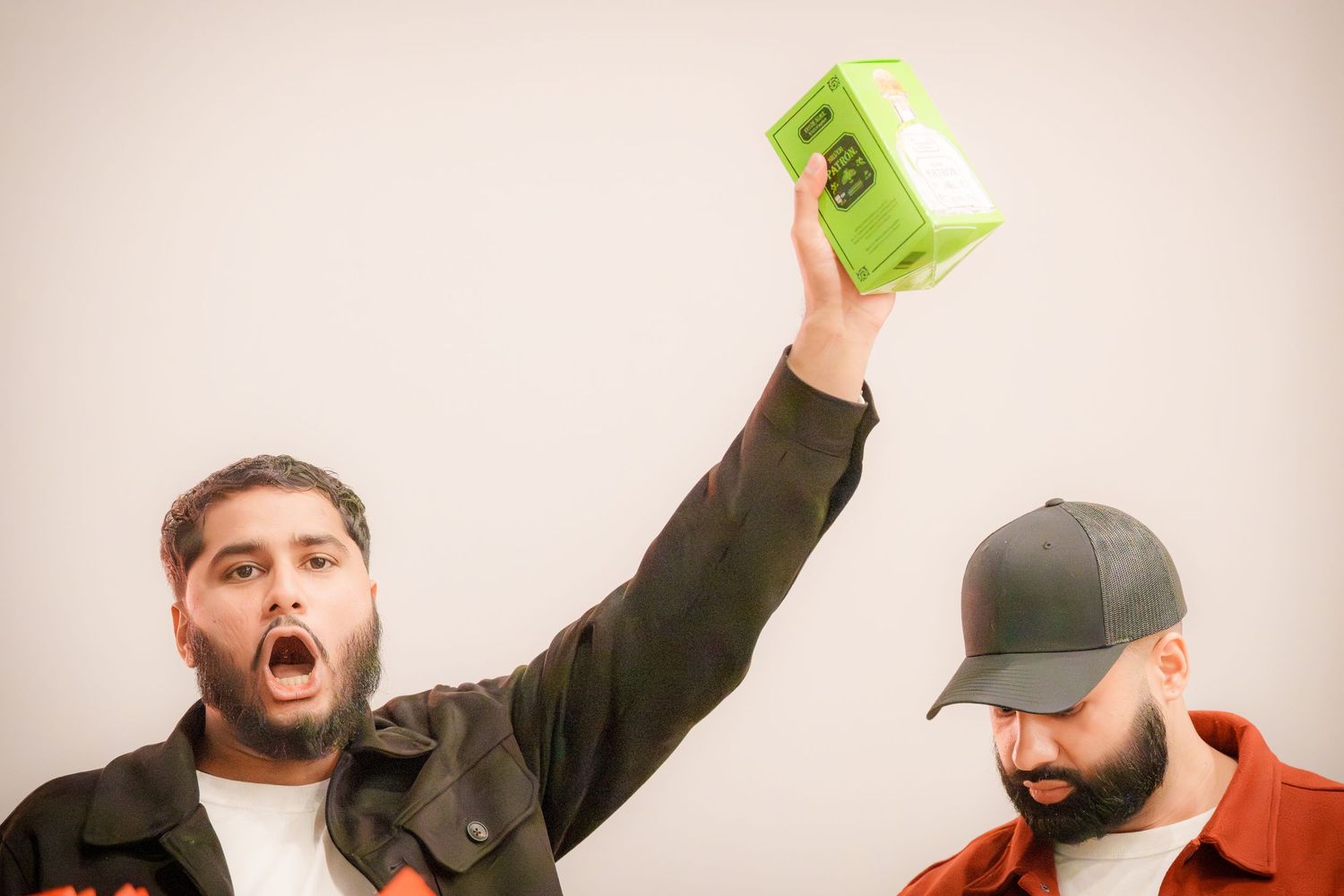 Person in dark clothing holds up a green package with excitement at a party.