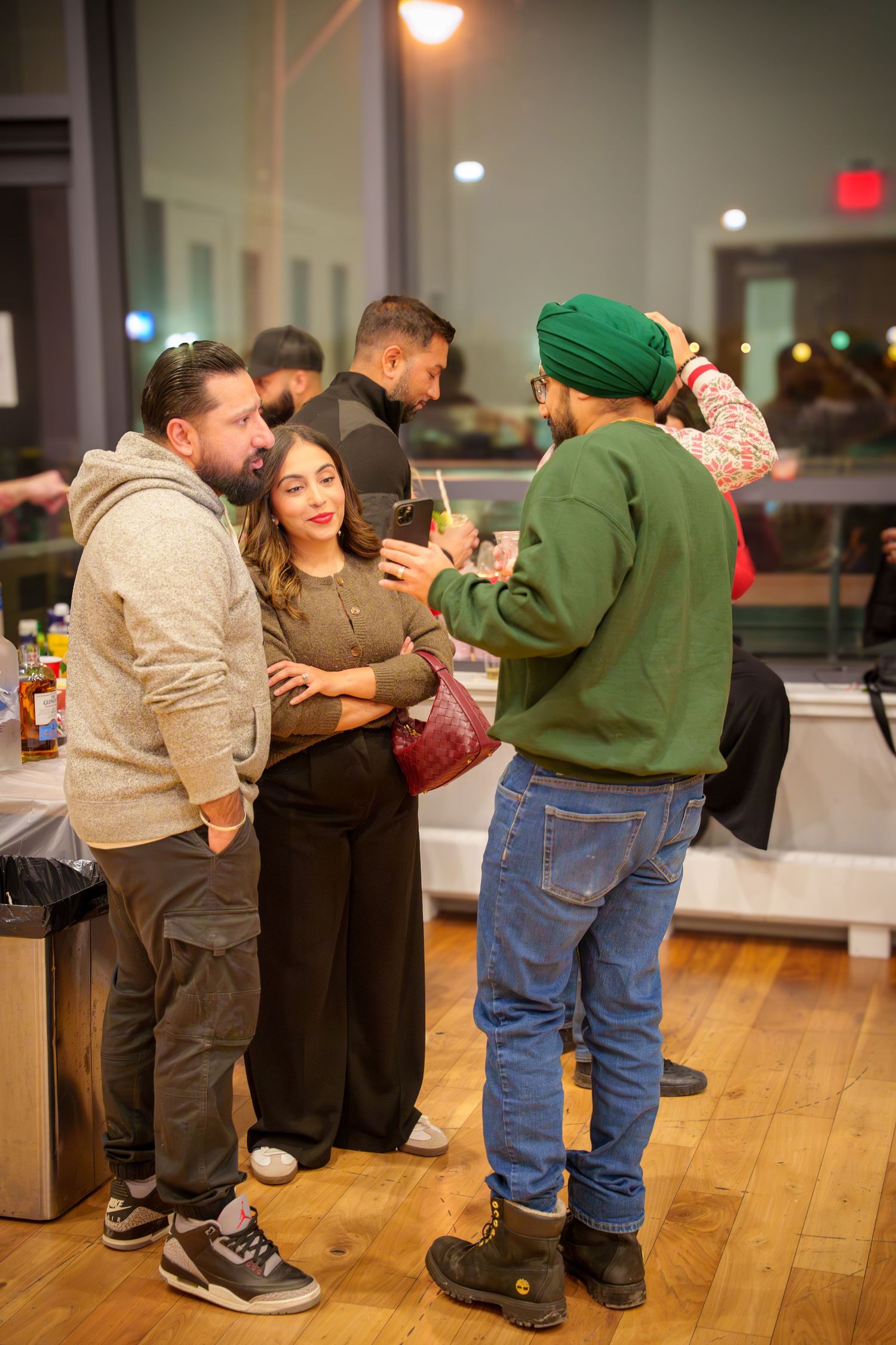 Group of friends enjoying drinks and conversation at a casual indoor party with wooden floors.