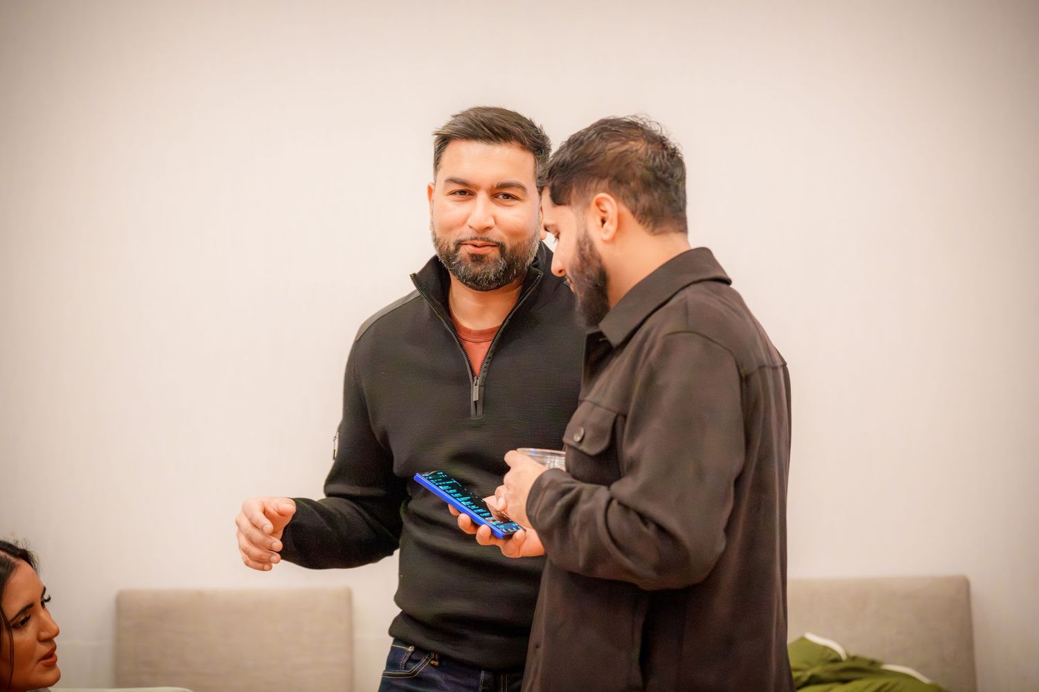 Two people engaged in conversation while holding drinks at an indoor gathering.