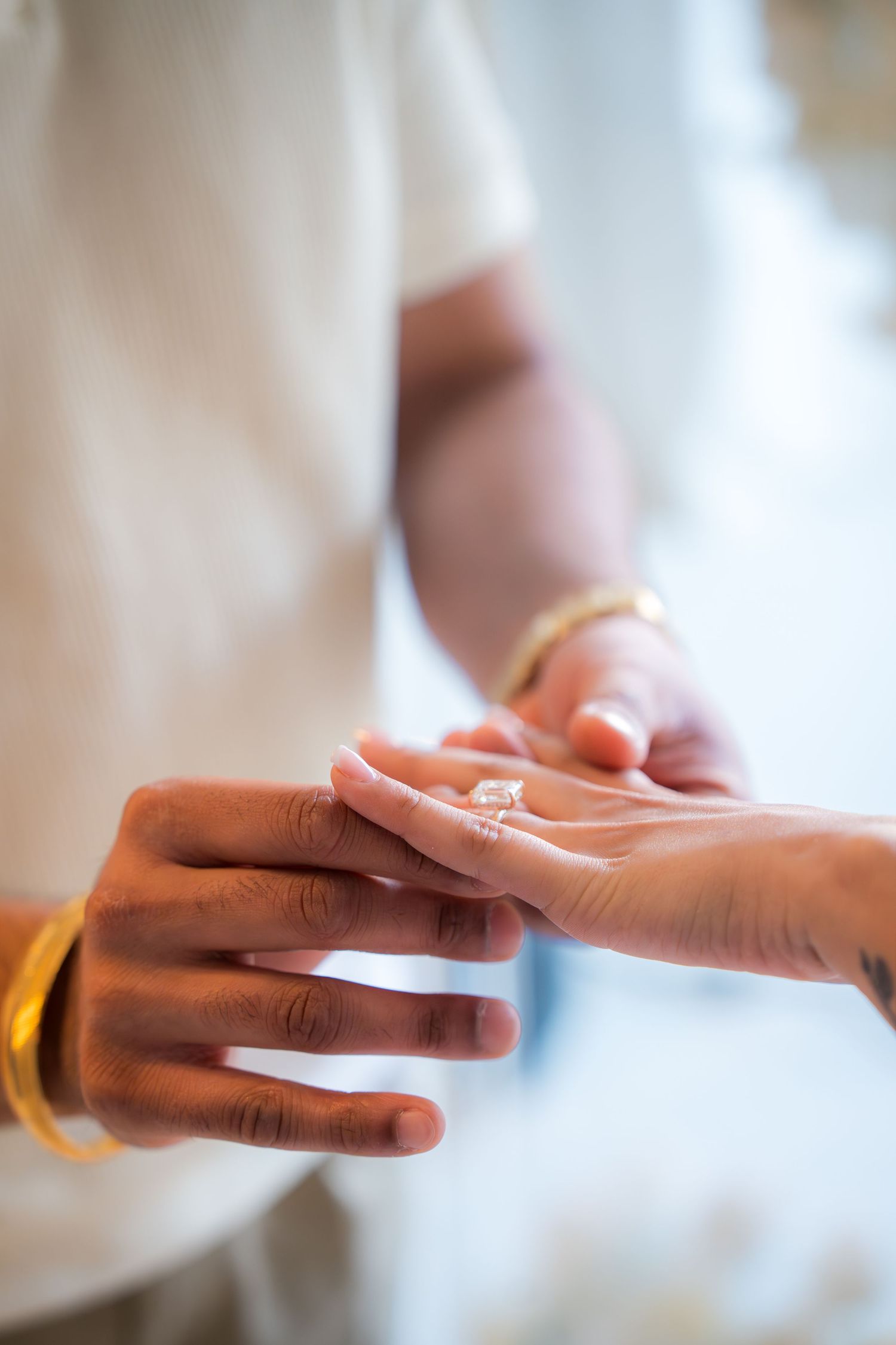 Groom placing diamond engagement ring on bride's finger during proposal ceremony.
