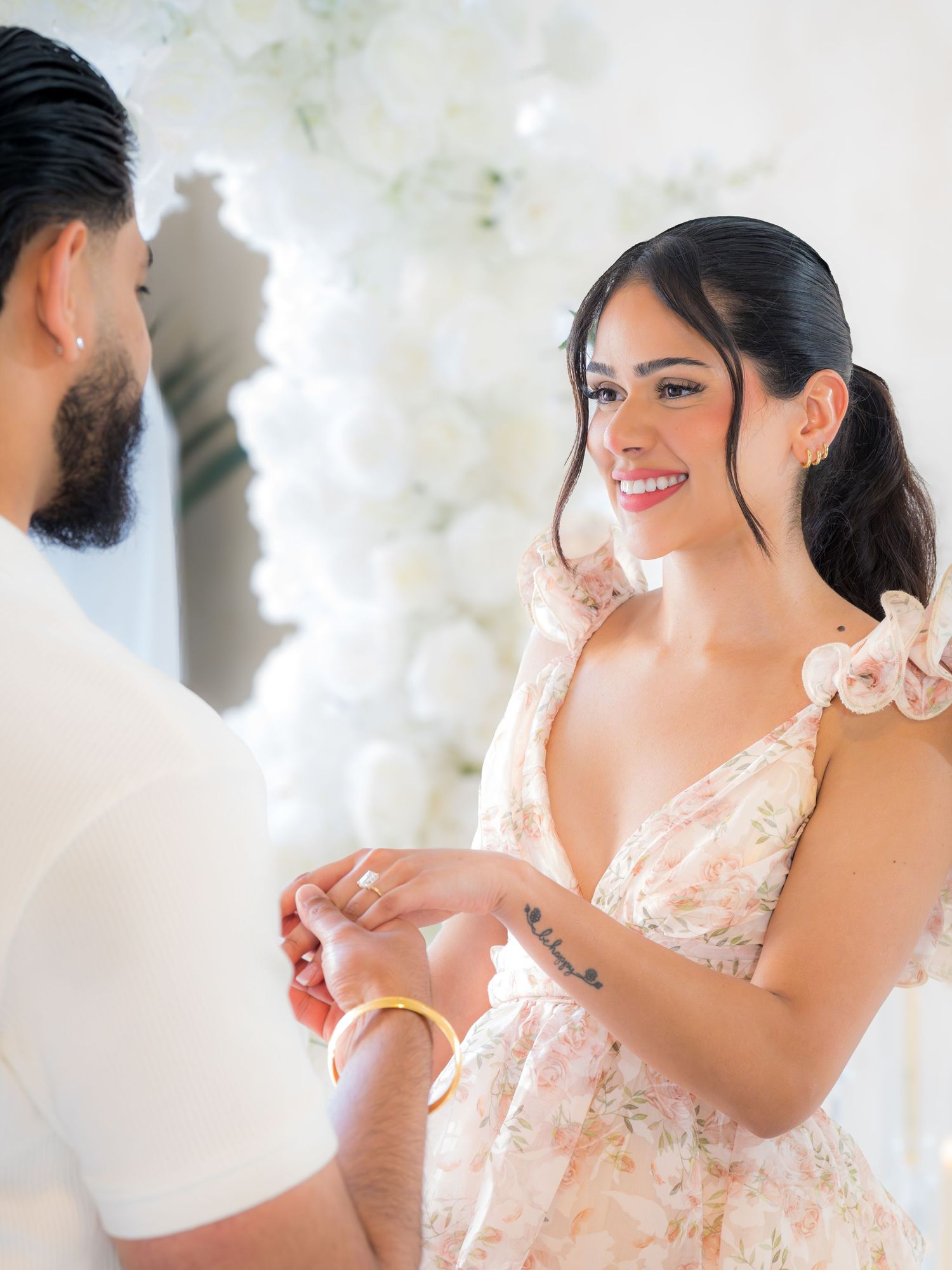 Man placing engagement ring on laughing woman's finger at floral decorated proposal.