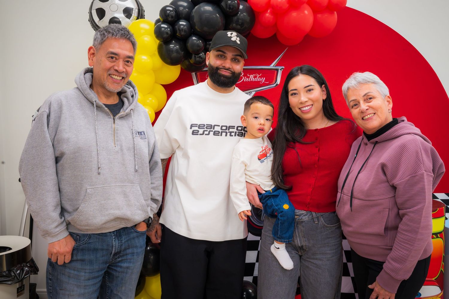 Family of five posing together at a racing-themed birthday party with colorful balloon decorations.