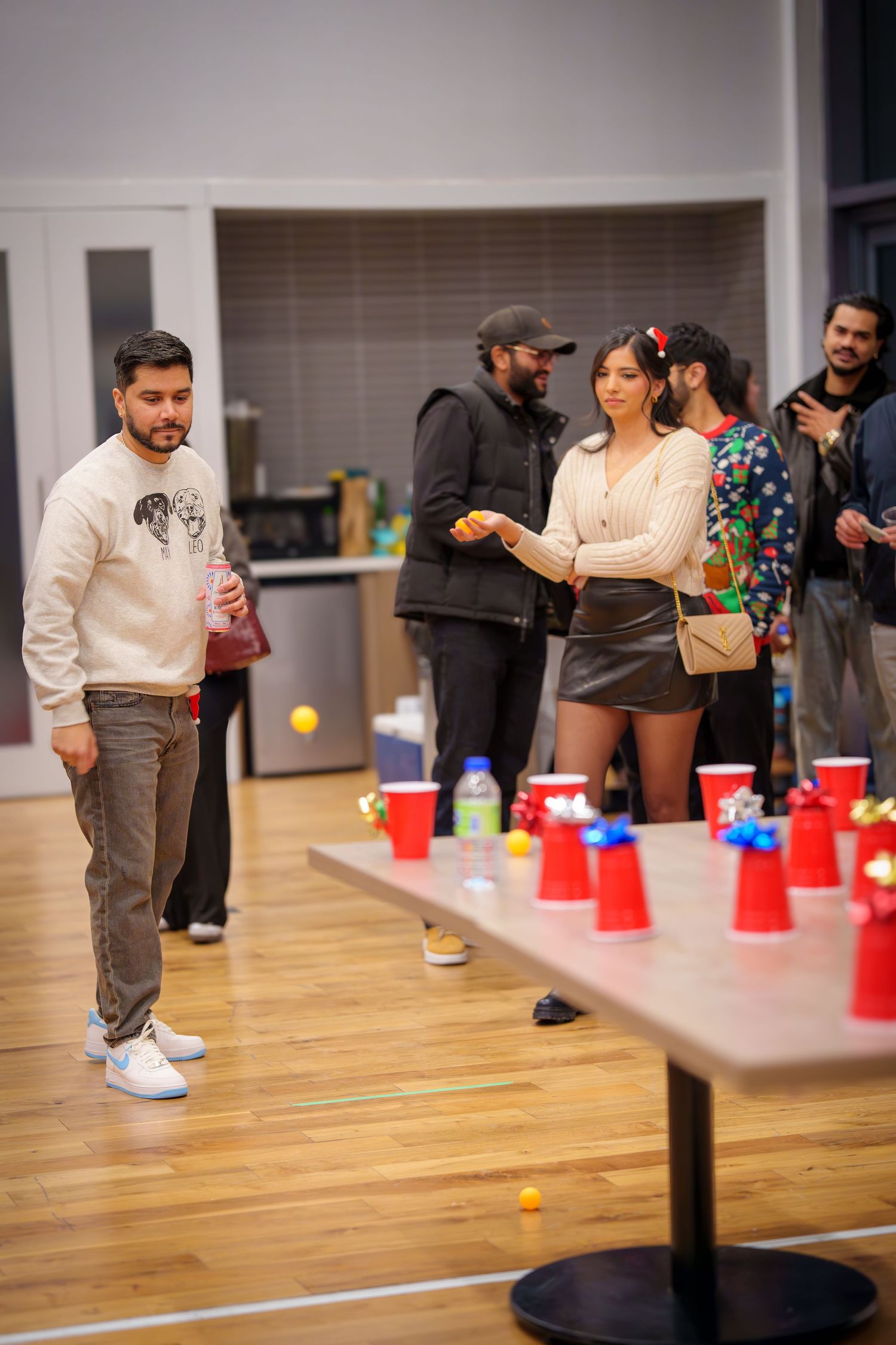 People playing a party game with red cups and ping pong balls on a wooden floor.
