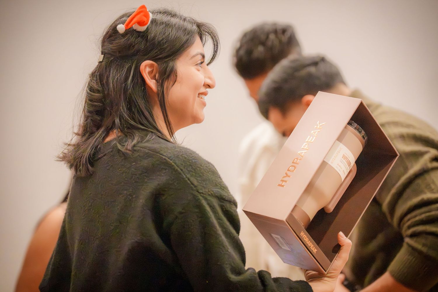People sharing laughter while holding gift boxes at an indoor social gathering.