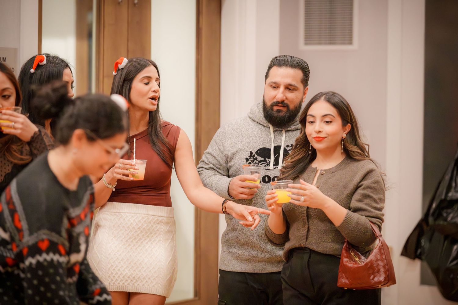 Party guests enjoy drinks and conversation at an indoor holiday celebration.