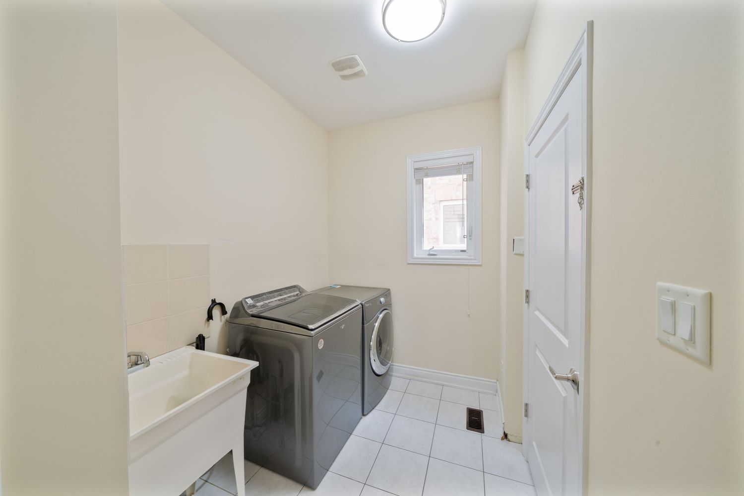 Long white hallway with tiled floor and recessed lighting leads to bathroom with window at the end.
