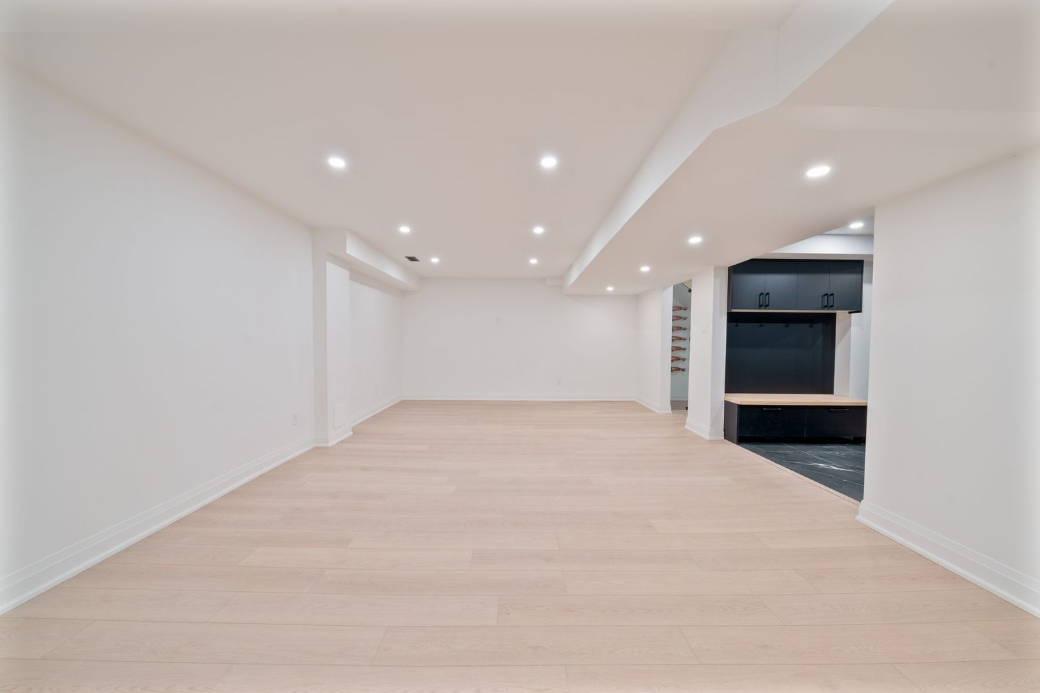 Modern white hallway with recessed lighting and glossy floors leading to an open space.
