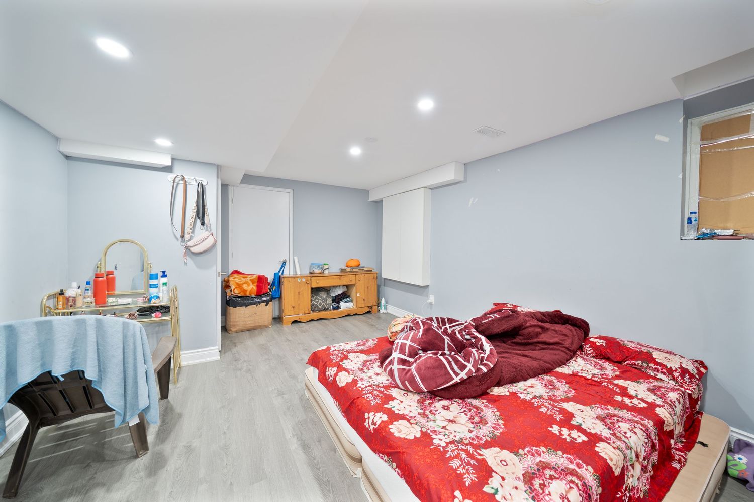 Modern basement bedroom features red floral bedding and white walls with recessed lighting illuminating the space.