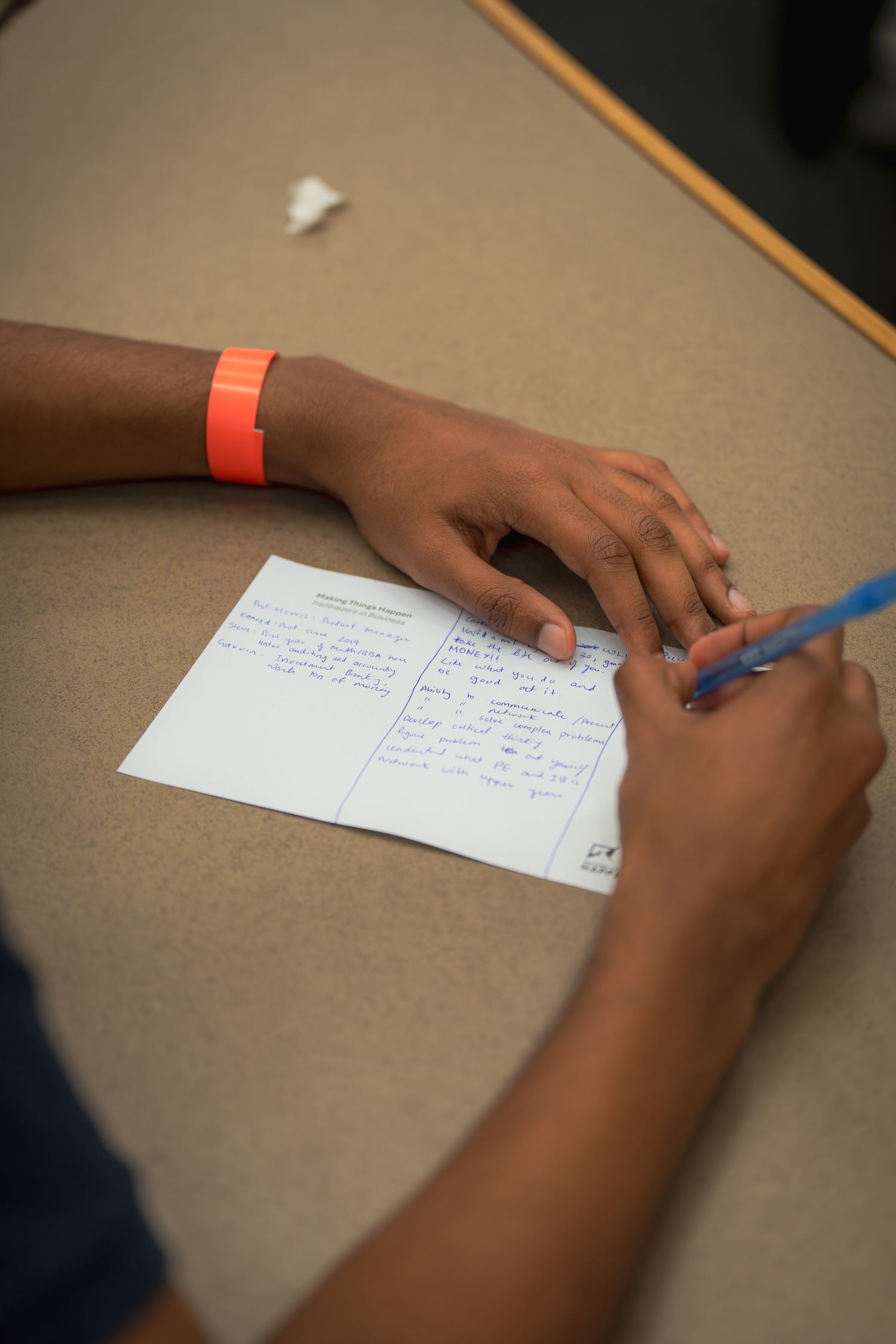 Close-up shot of hands writing notes on paper at a desk during a meeting or study session.