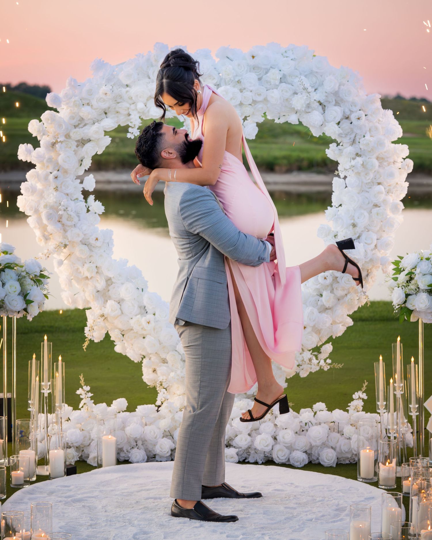 Wedding couple sharing a romantic dip pose under a white floral arch with candles.