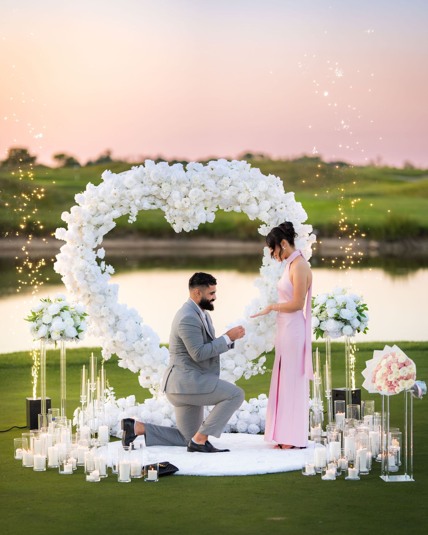 Intimate proposal moment captured under a white floral arch with candlelit decorations.