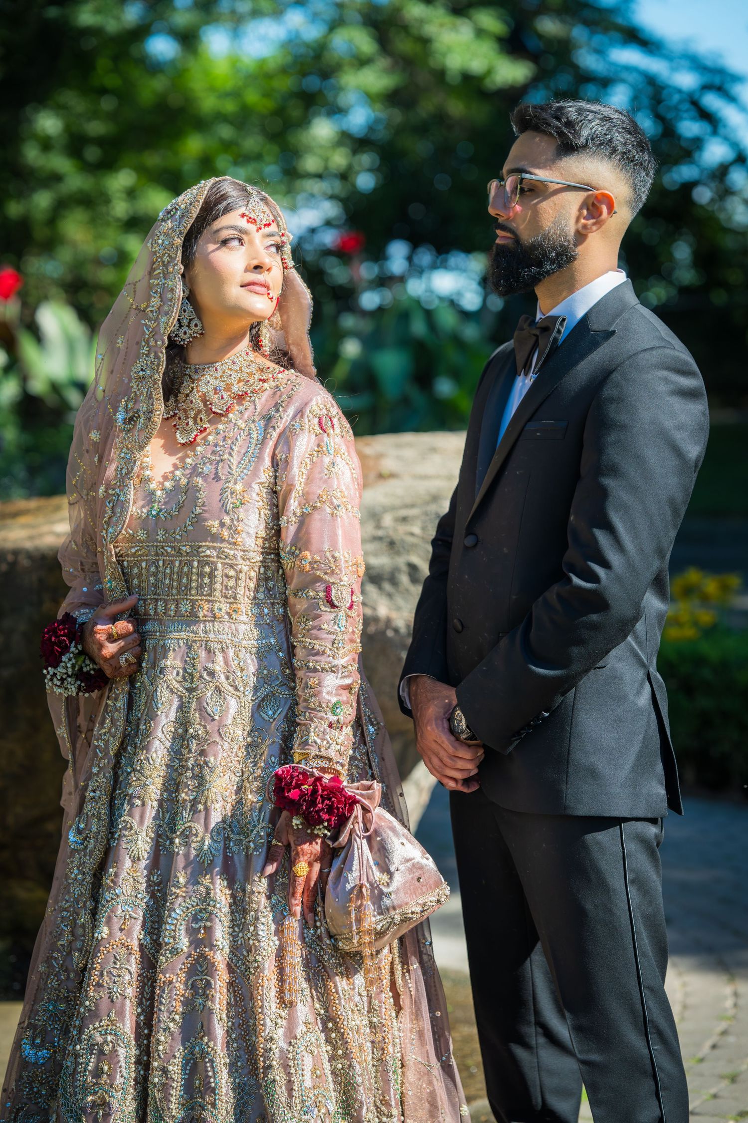 A couple shares romantic moments in traditional South Asian wedding outfits against a natural backdrop.
