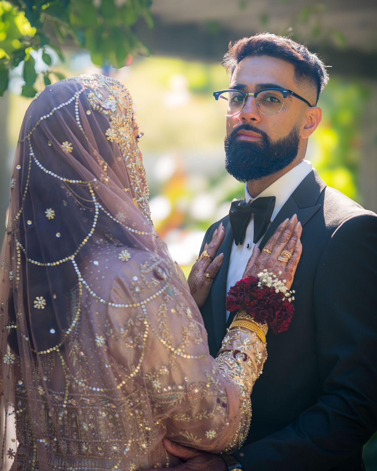 A romantic wedding portrait showing traditional South Asian bridal attire with intricate beadwork and a dapper groom in black.