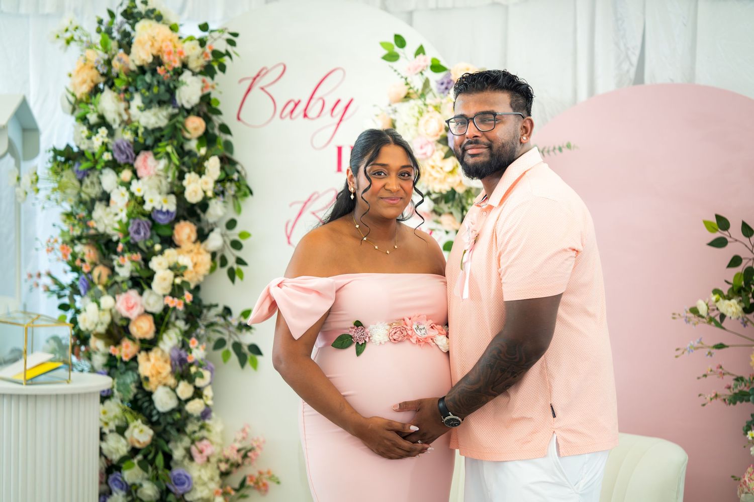 A couple poses together against a romantic backdrop with pink roses and greenery.