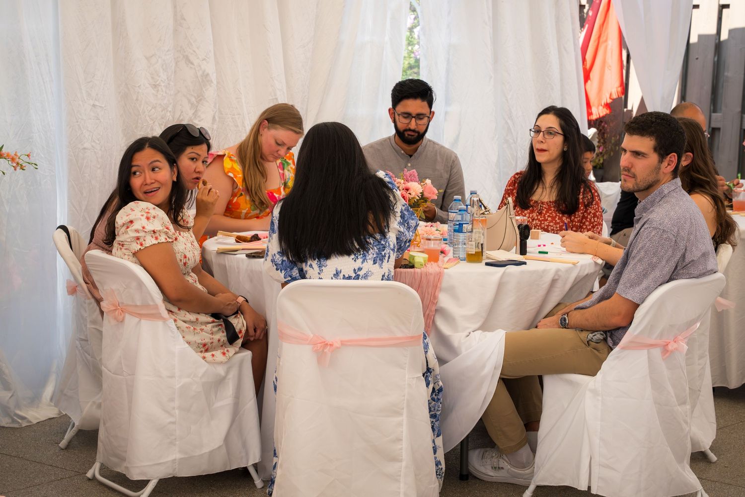 Guests enjoying food and drinks at a baby shower celebration with white chair covers and pink decor.