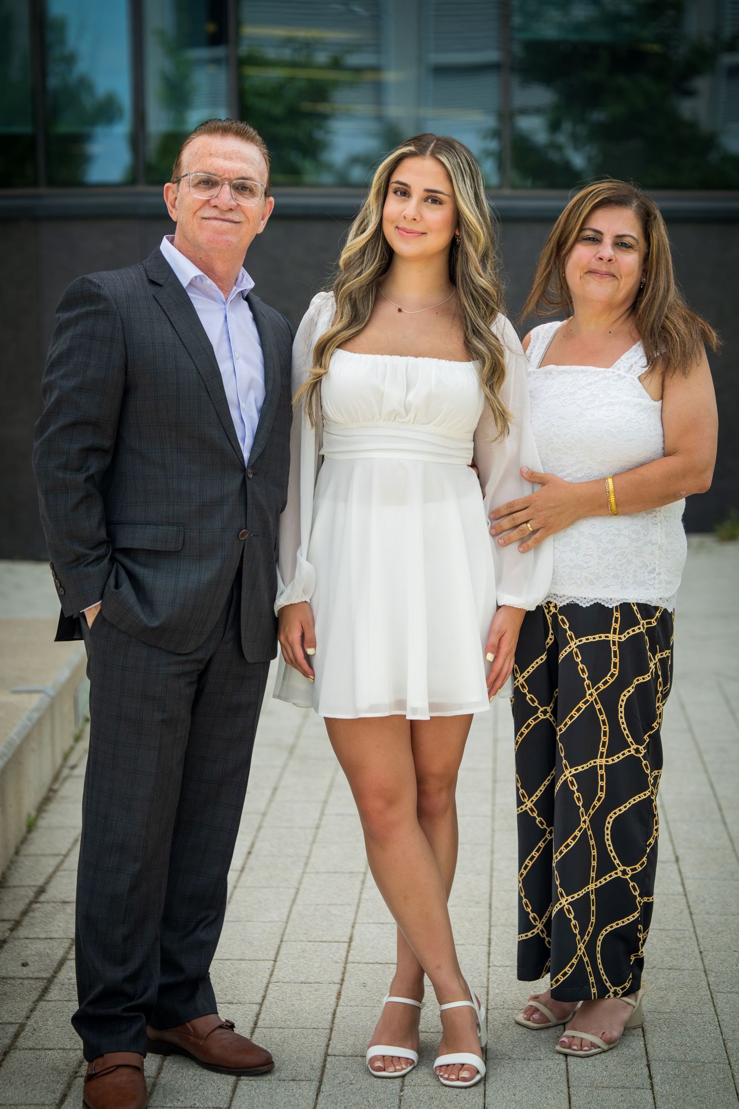 Three people pose together outdoors wearing contrasting white and black formal attire.