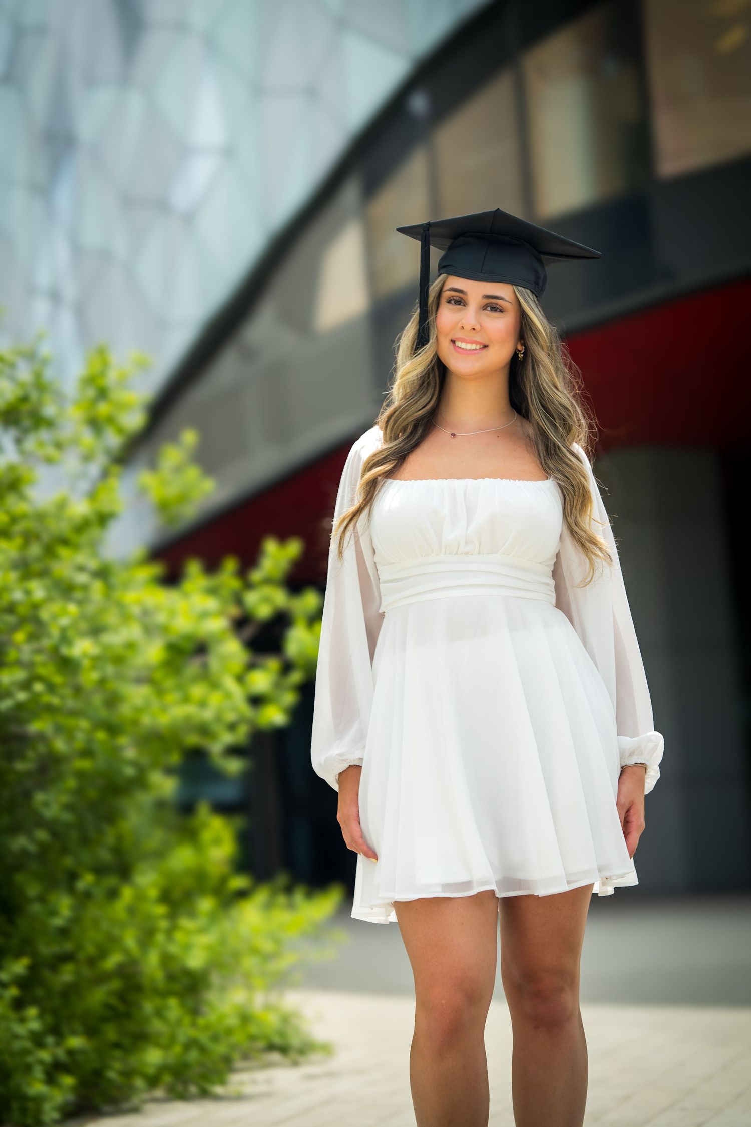 Outdoor graduation portrait featuring white dress against modern architecture.