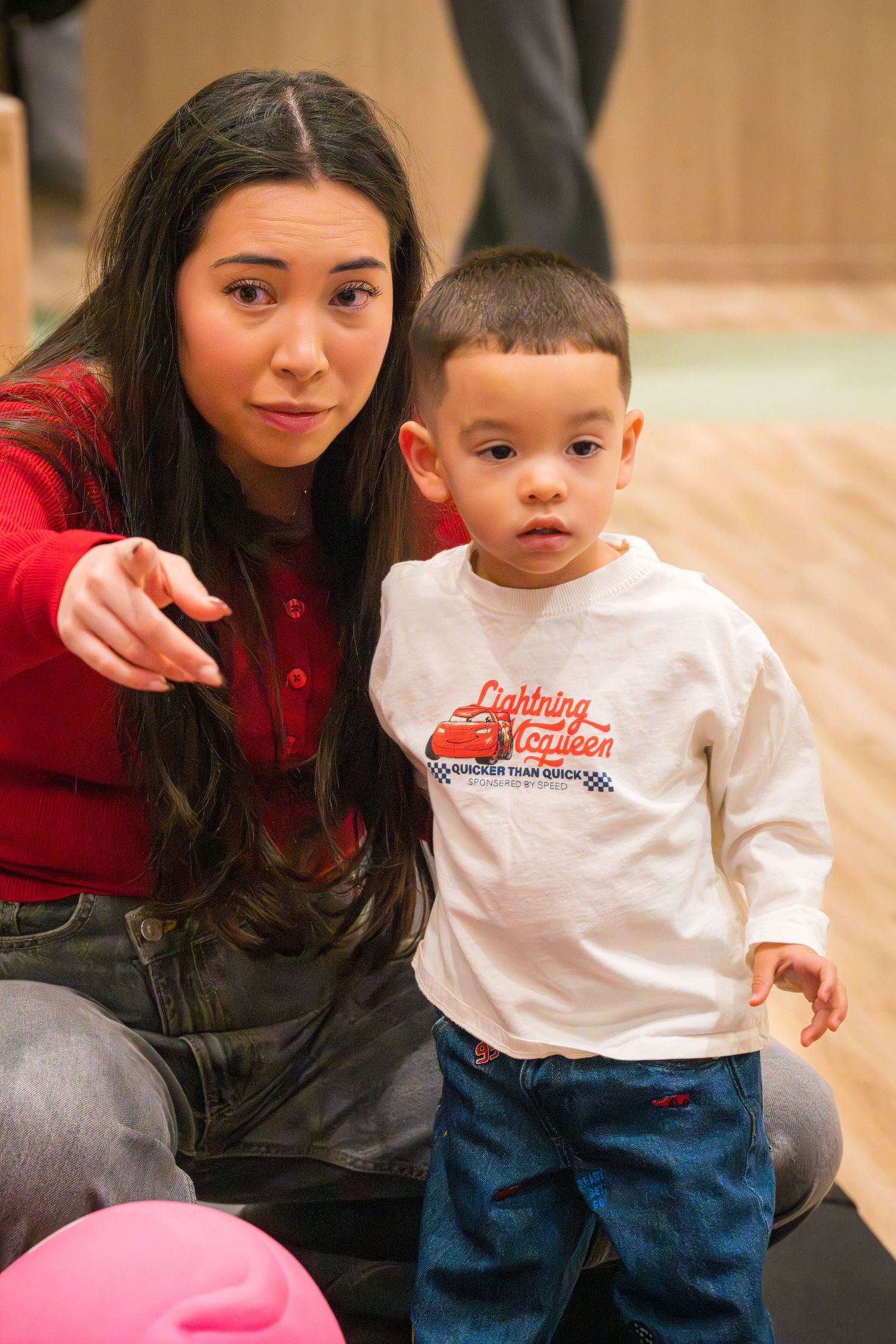 A young woman in red crouches beside a toddler boy wearing a Lightning McQueen shirt.